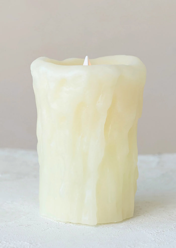 A flameless electronic pillar candle in natural color with drippy appearance.