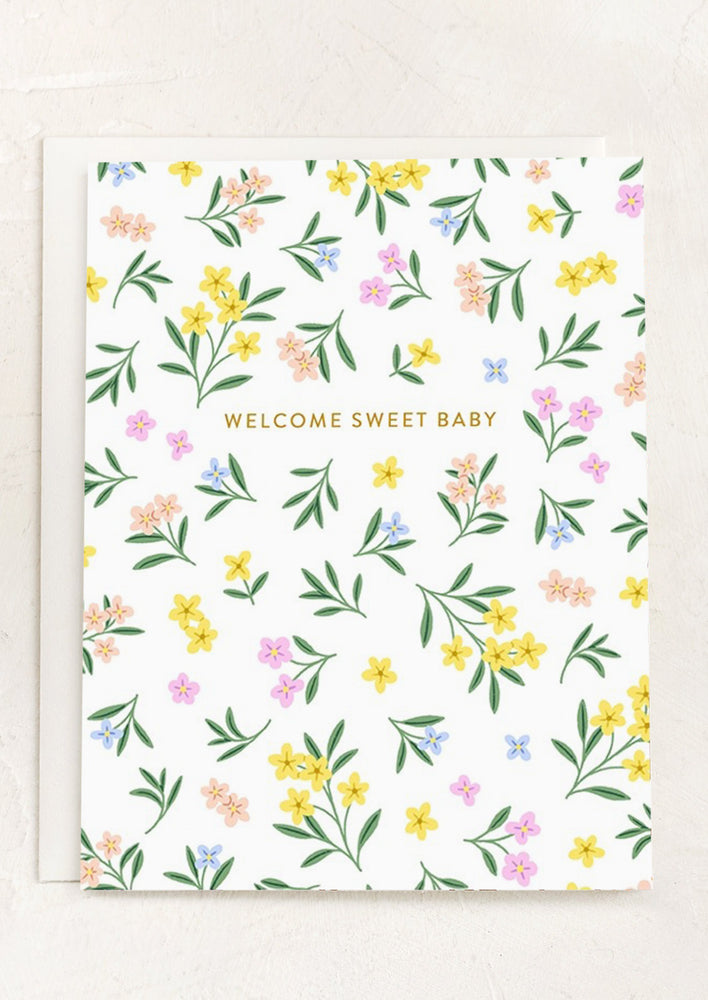 A greeting card with pastel floral pattern, text reads "Welcome sweet baby".