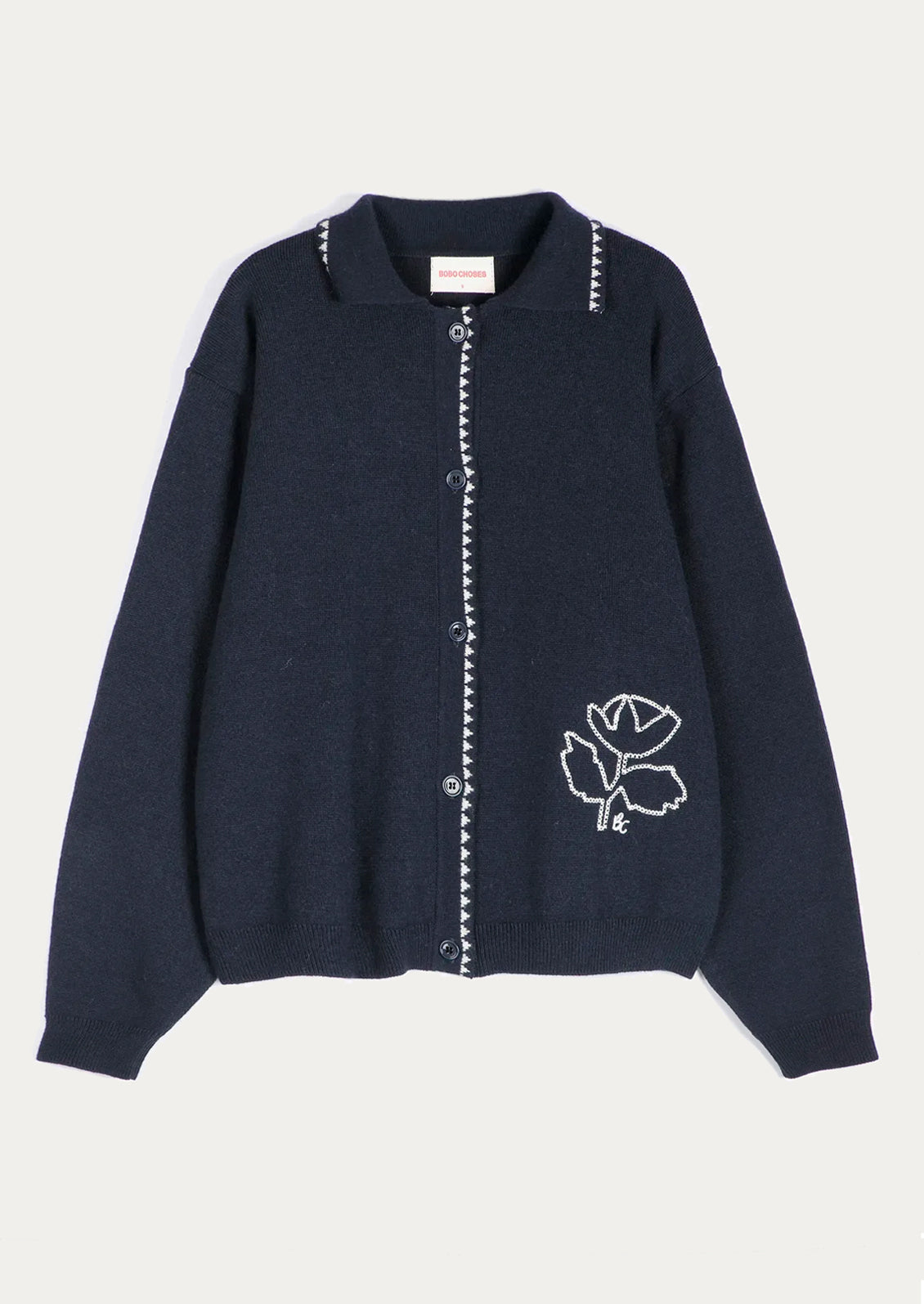 A dark navy blue knit cardigan sweater with white embroidered details, including a rose motif on the lower right side and decorative trim along the collar and front button placket, shown against a light off-white background.