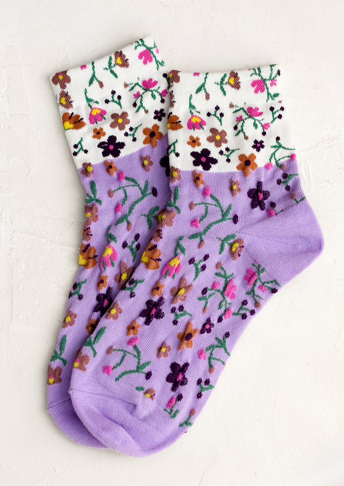 A pair of two-tone socks in white and purple with multicolor flower pattern.