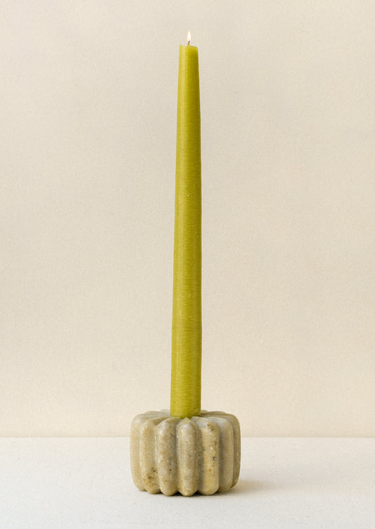 A fluted marble taper holder with a long green taper candle.