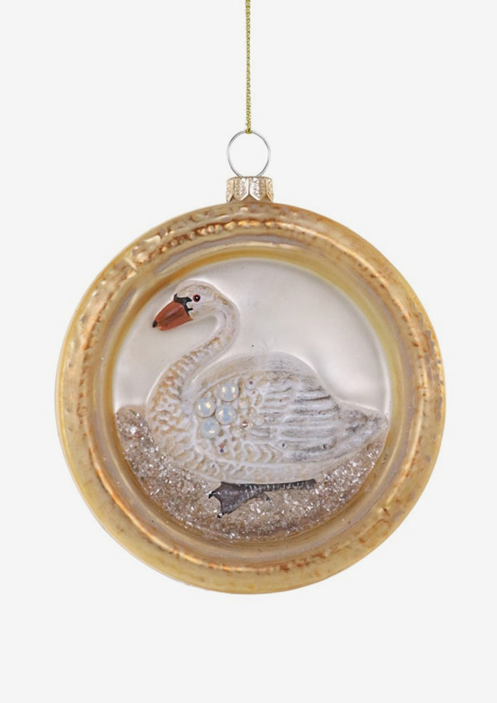A glass ornament of a round frame around white swan.