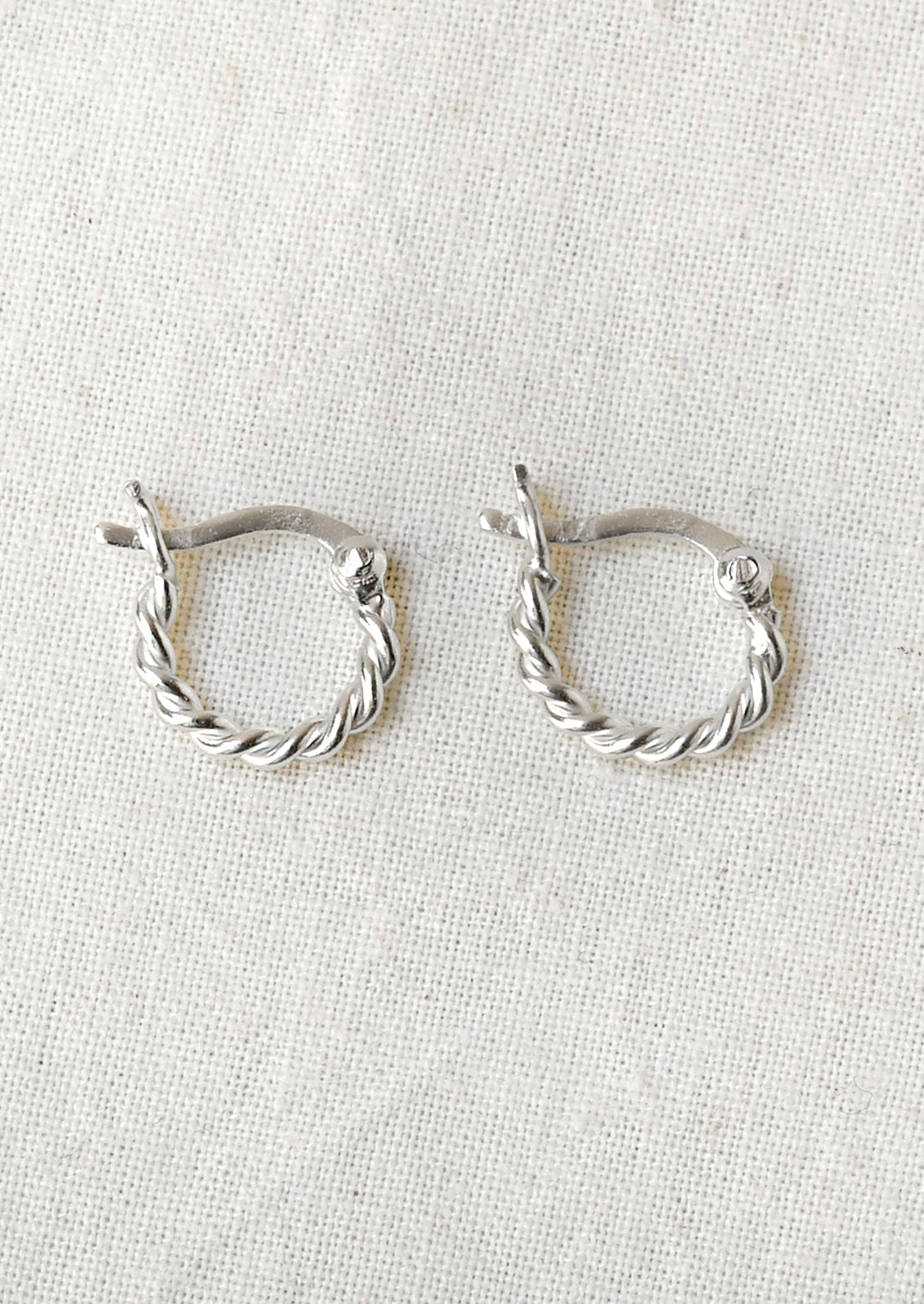 A pair of small silver hoop earrings with a twisted design.