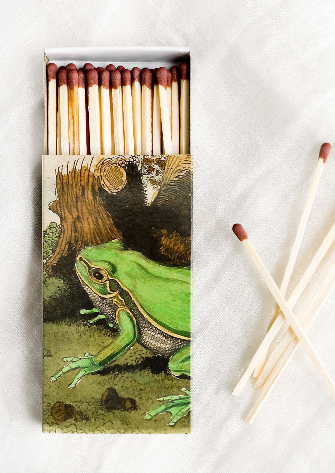 A frog print matchbox with long, brown-tipped matches.