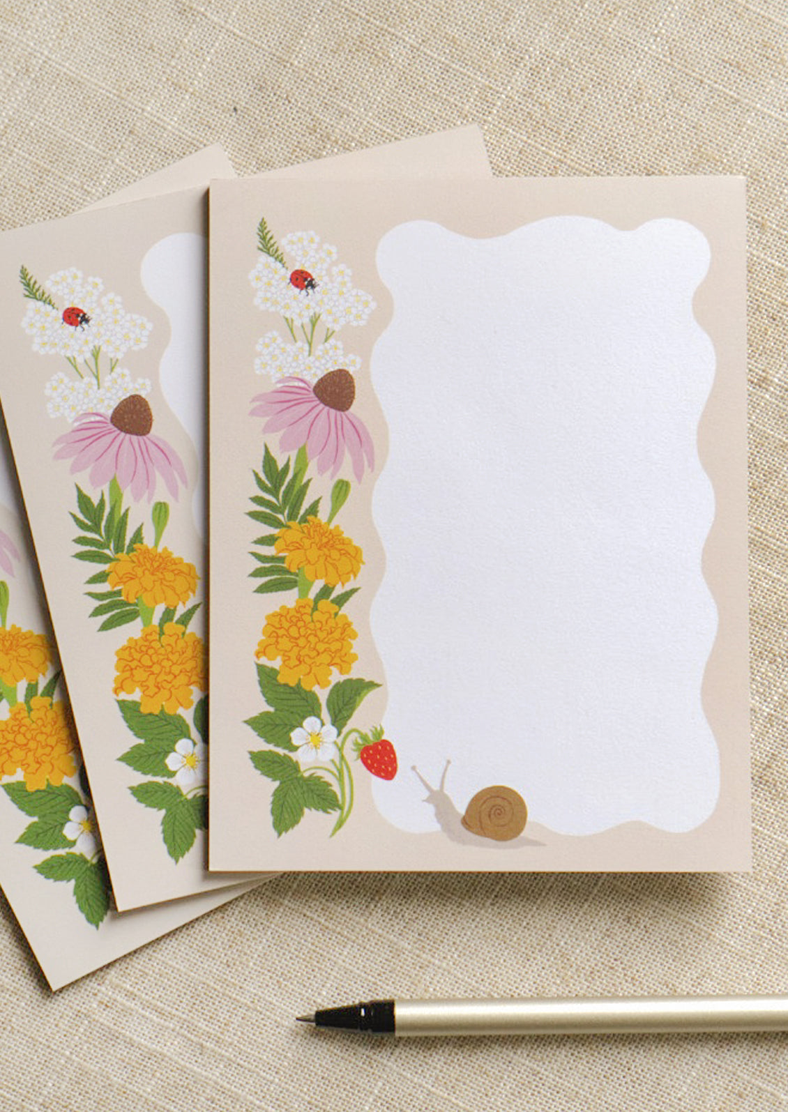 Three notepads stacked in a staggered fashion with a ripple white section and an illustration of a happy snail and ladybug enjoying yarrow, marigold, coneflower, and fresh strawberries.
