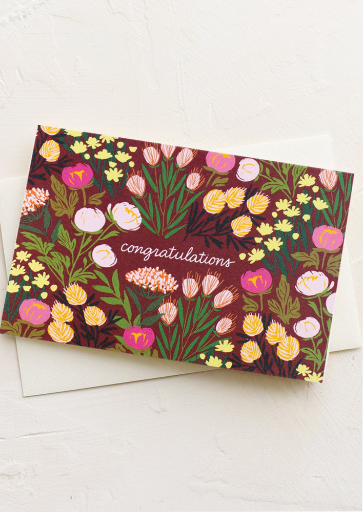 A card with dark red floral pattern with text reading "Congratulations".