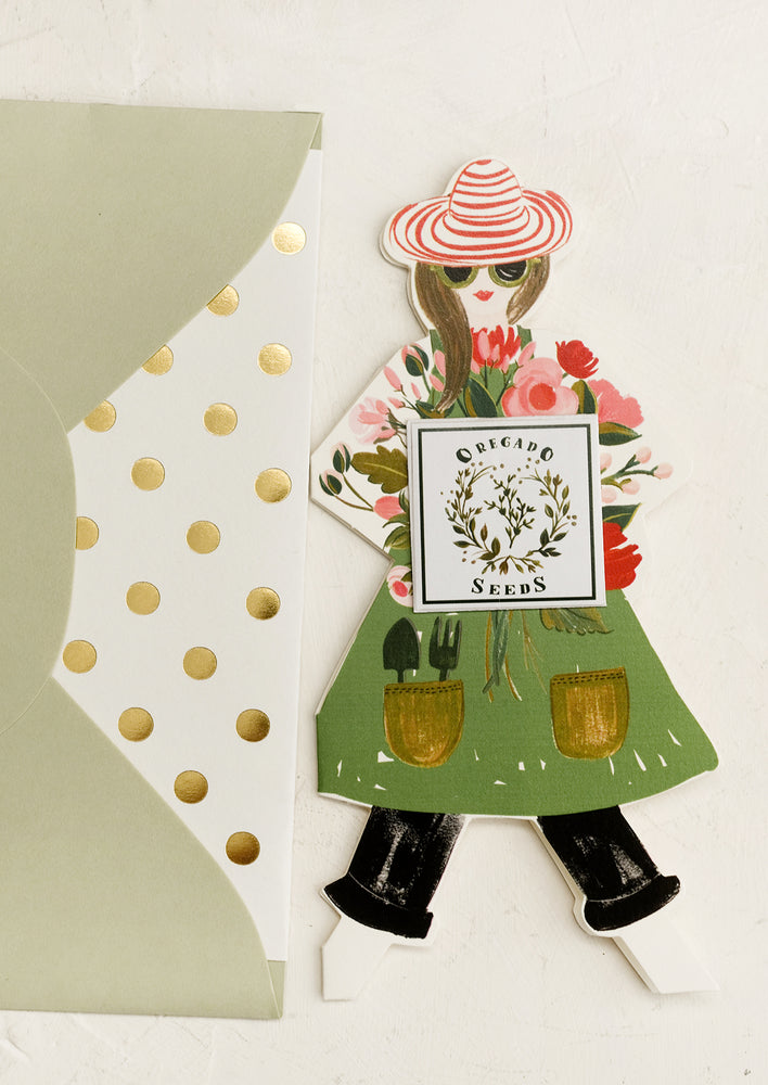 A diecut card in the shape of a woman, who is dressed as a gardener and is holding a packet of oregano seeds.