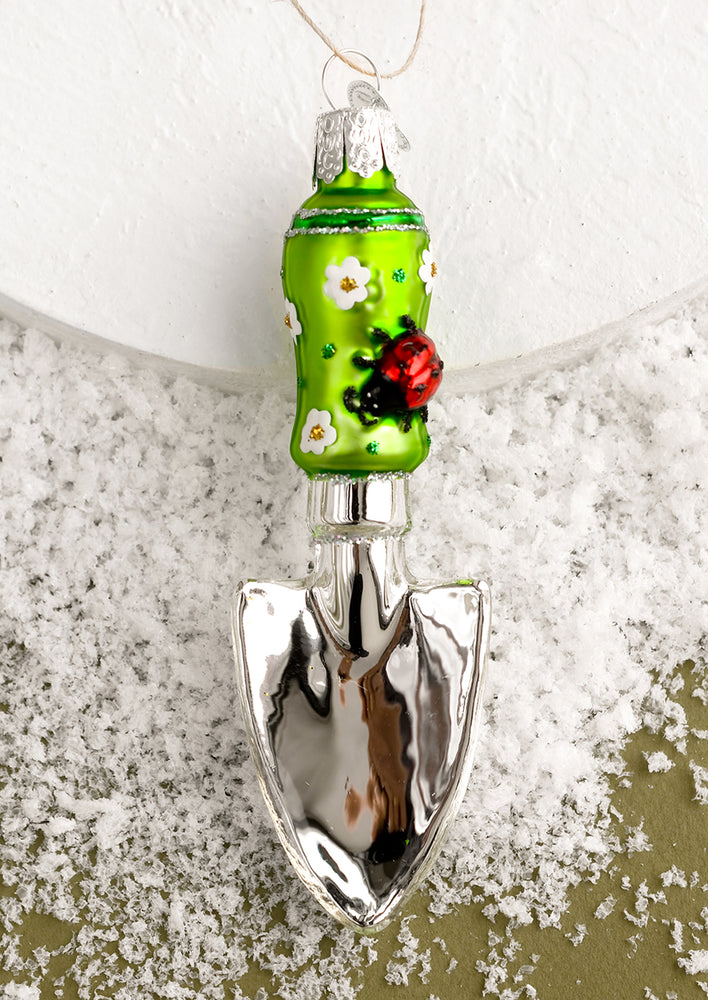 A glass holiday ornament of a gardening trowel.