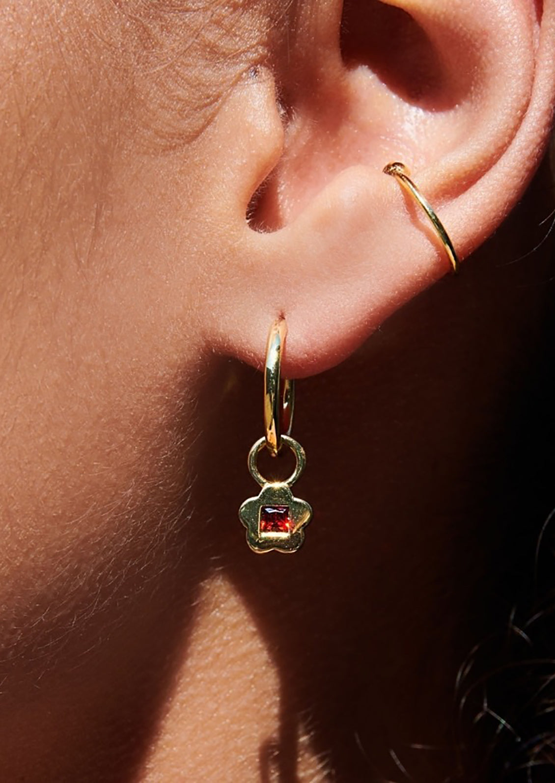 A pair of gold hoop earrings with garnet flower charm.