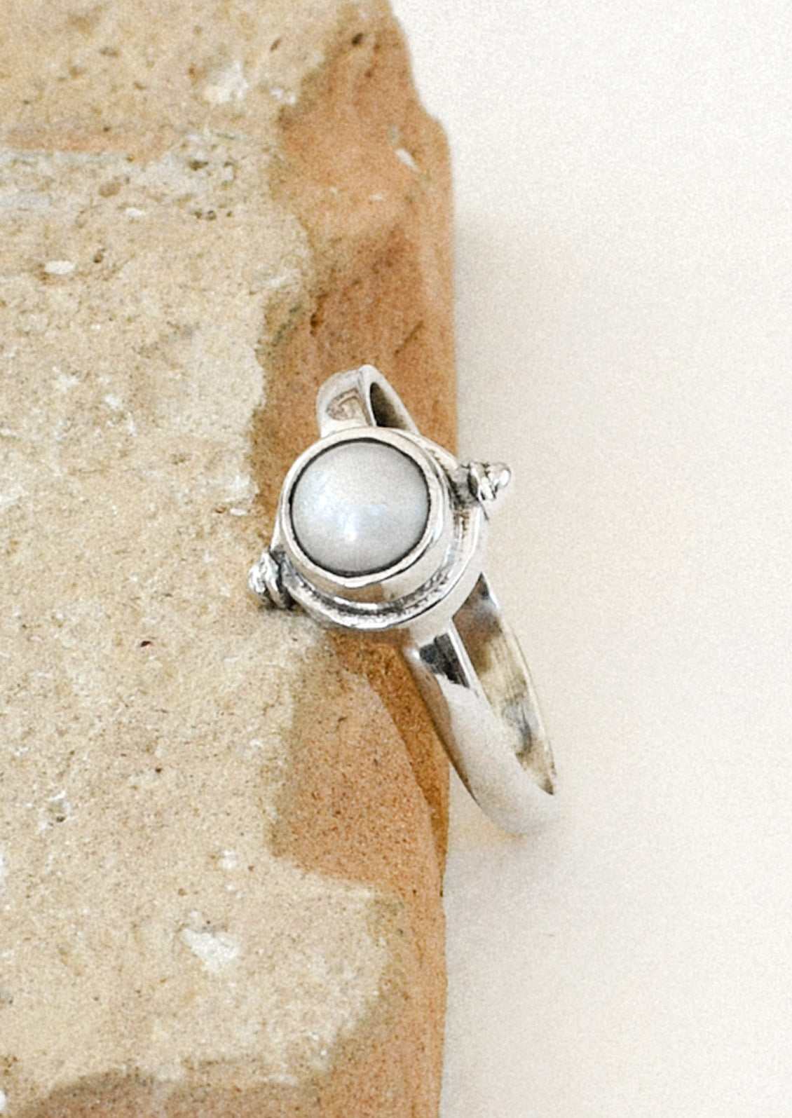 A sterling silver ring with a faux pearl in the center leaning on a brown stone.