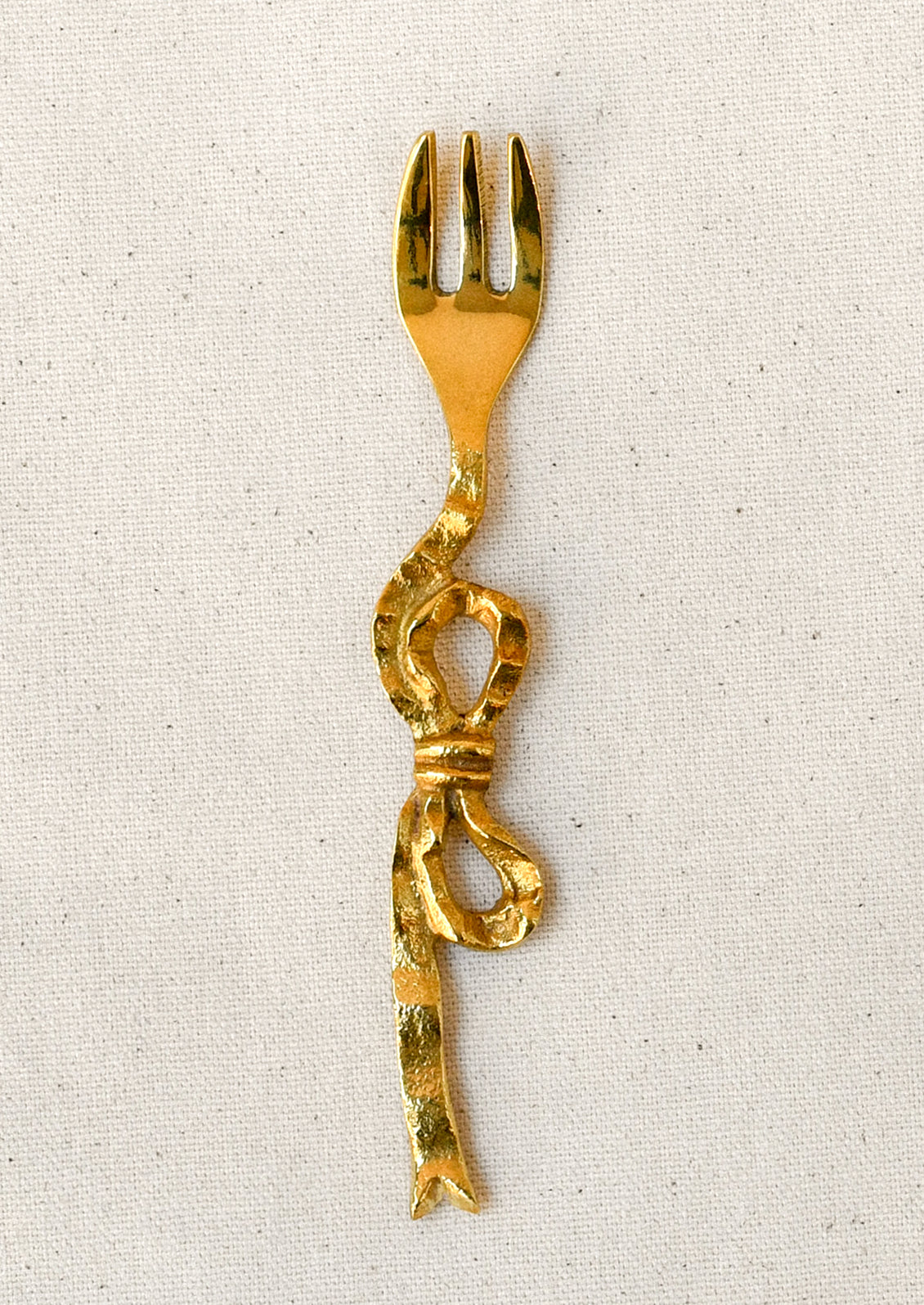 A brass canapé fork with a bow shaped design.