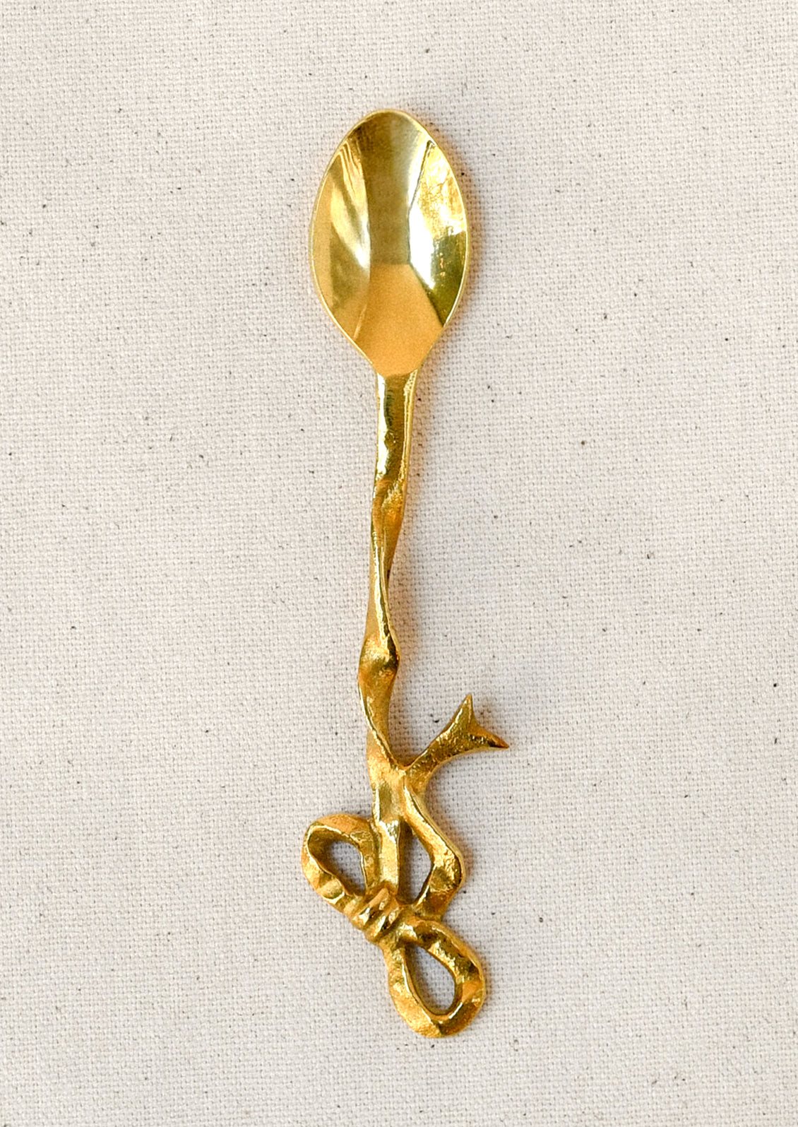 A brass canapé spoon with a bow shaped design.