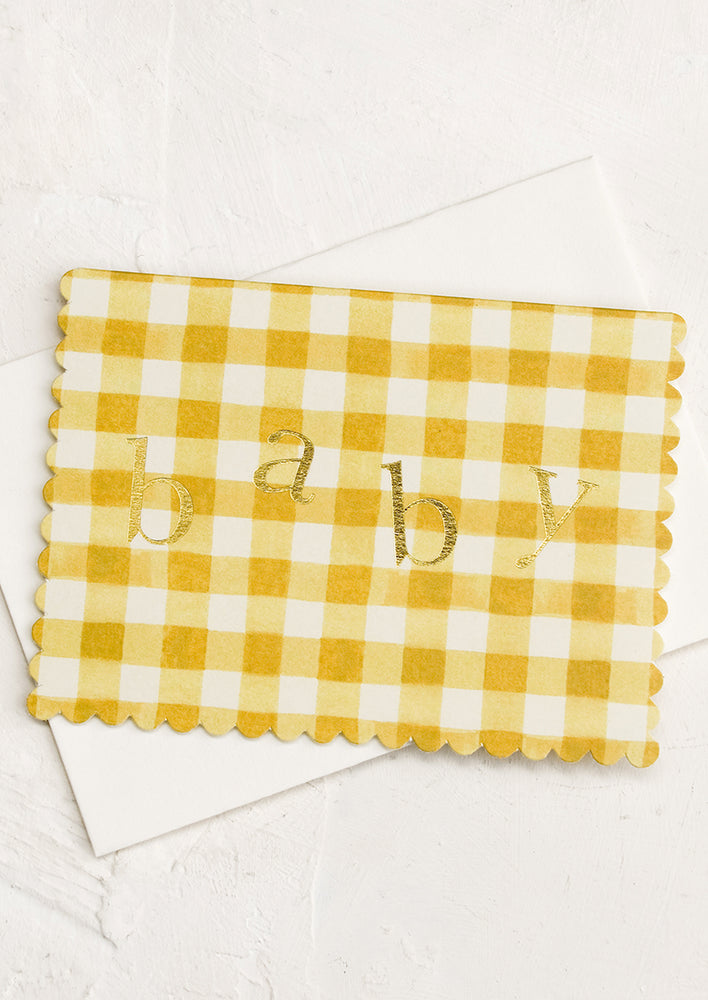 A yellow gingham pattered card with scalloped edges reading "baby" in gold lettering.