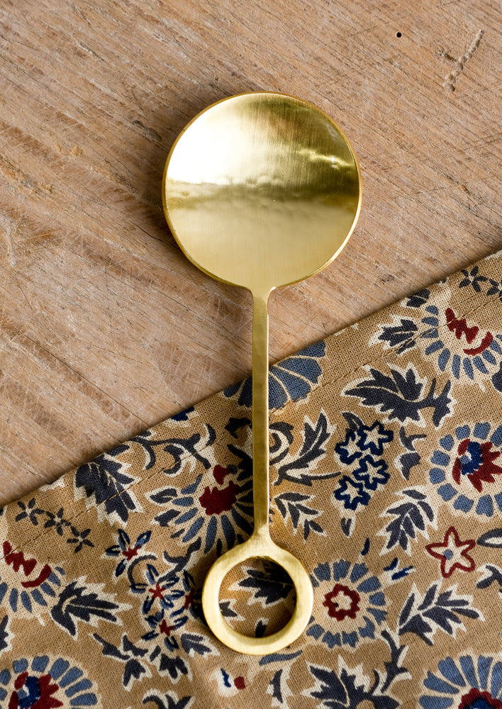 Gold finish dish spoon with circular loop at end of handle.