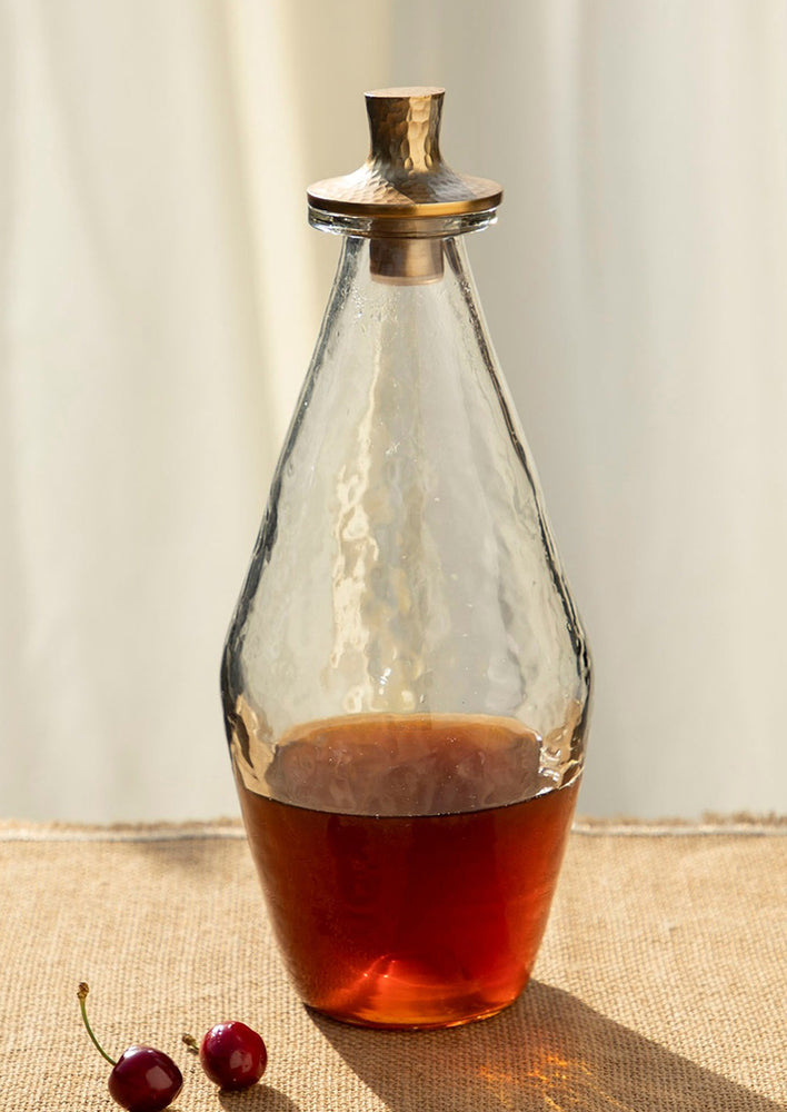 A hammered glass decanter with modern, tapered shape and brass lid.