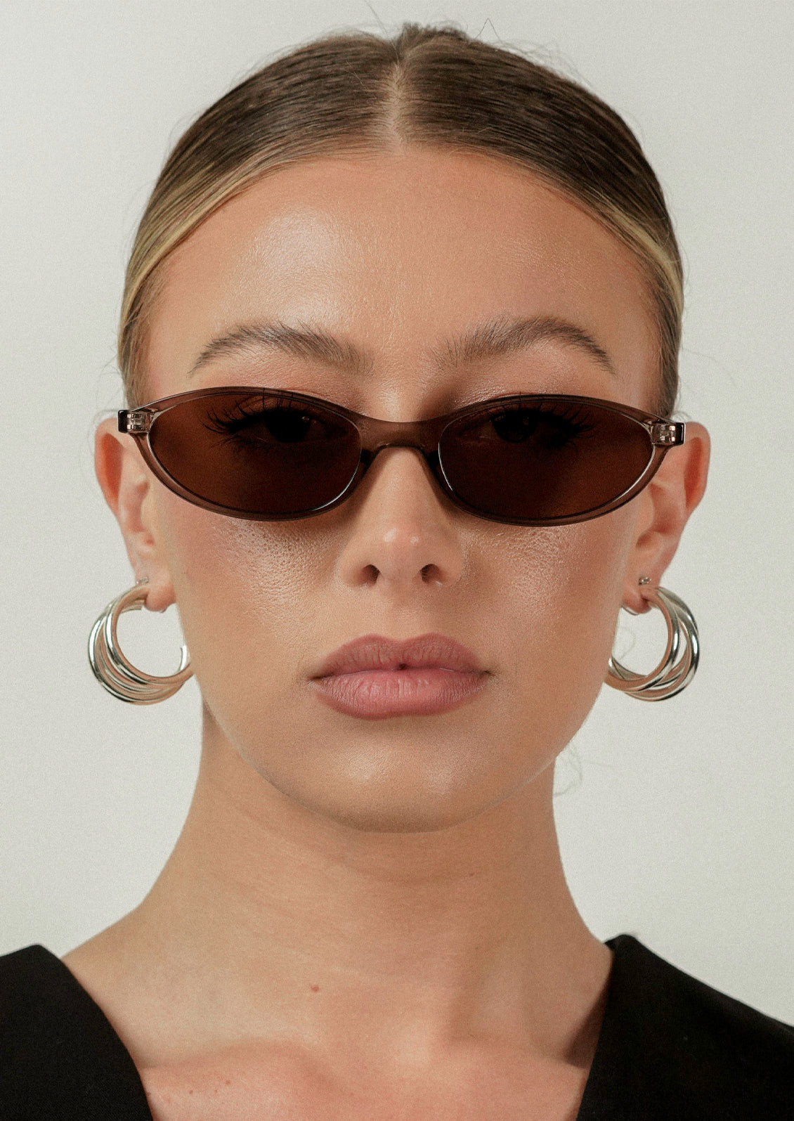 A woman wearing a pair of rounded cat eye sunglasses with a transparent olive frame and brown lenses.