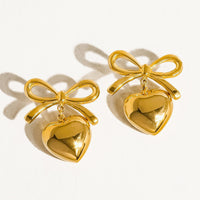 2: A pair of gold earrings with dangling heart charm and bow shaped post.