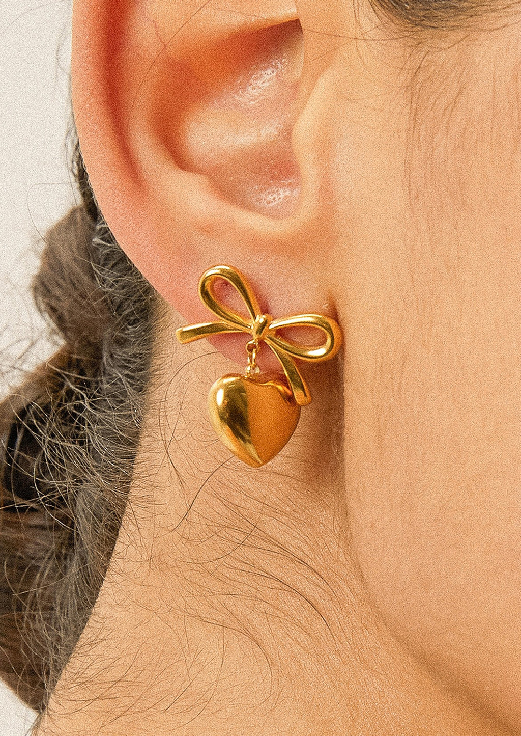 1: A pair of gold earrings with dangling heart charm and bow shaped post.
