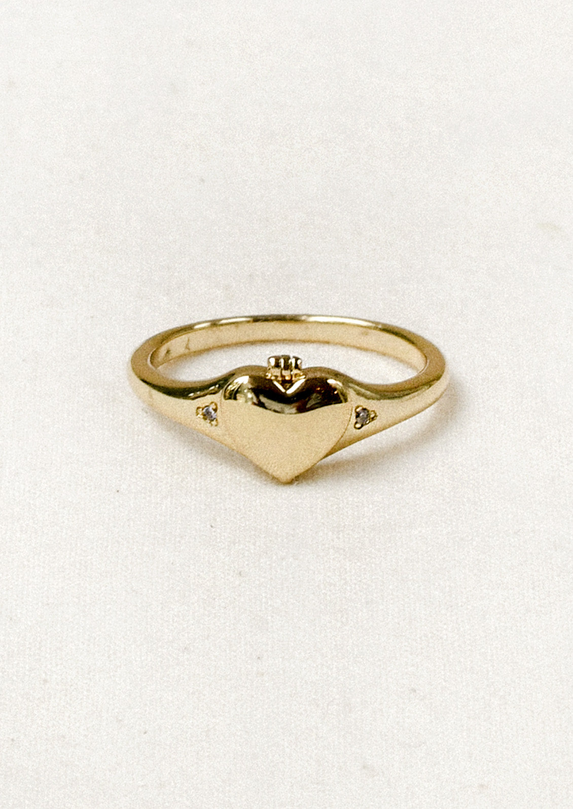 A gold ring with a tiny locket in the shape of a heart in the center and crystal detailing on either side.
