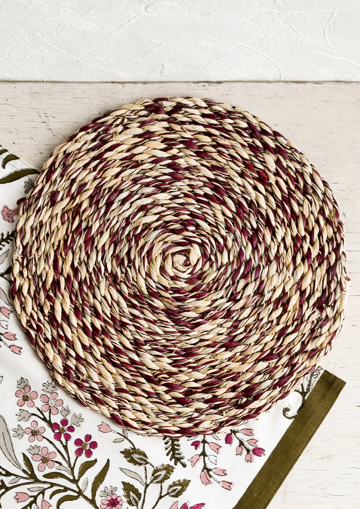 A round woven raffia placemat in natural and raisin.