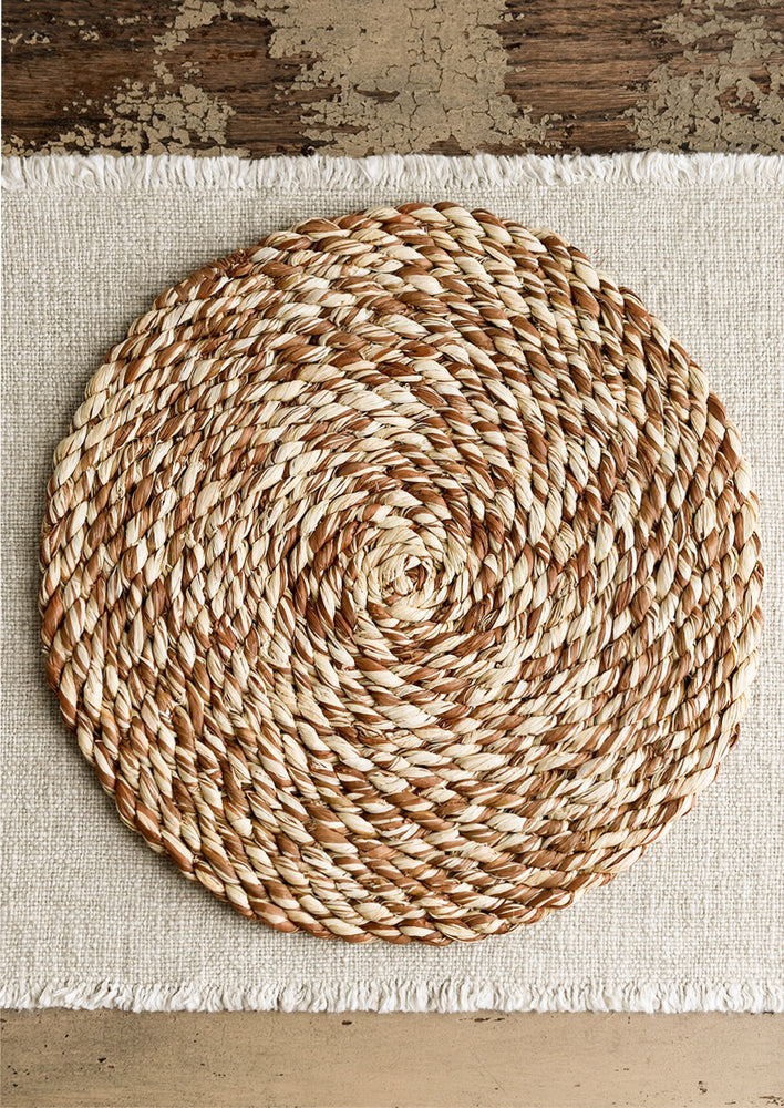 A round woven raffia placemat in natural and brown.