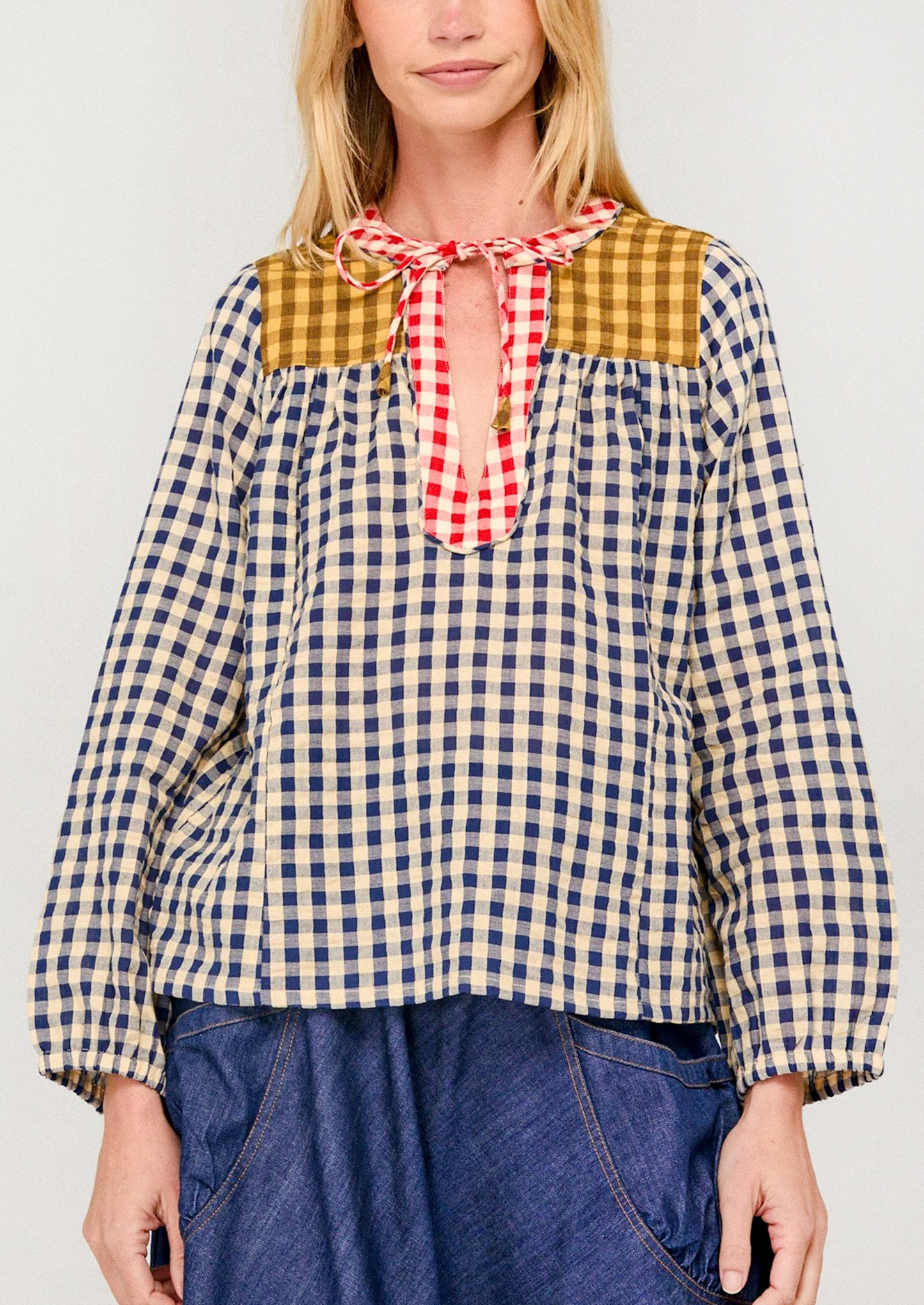 Woman wearing a checkered blouse with a red and white plaid bow tie against a plain background