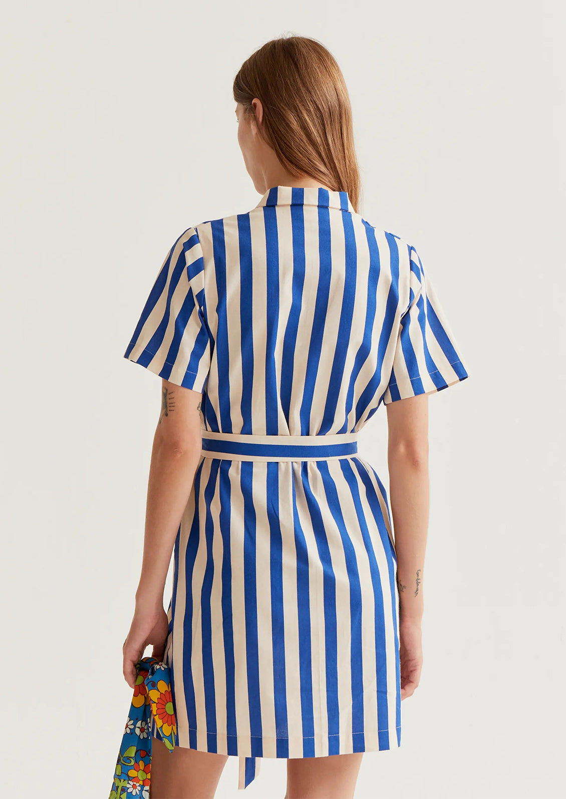 Woman wearing a blue and white striped dress holding a colorful bag on a light gray background