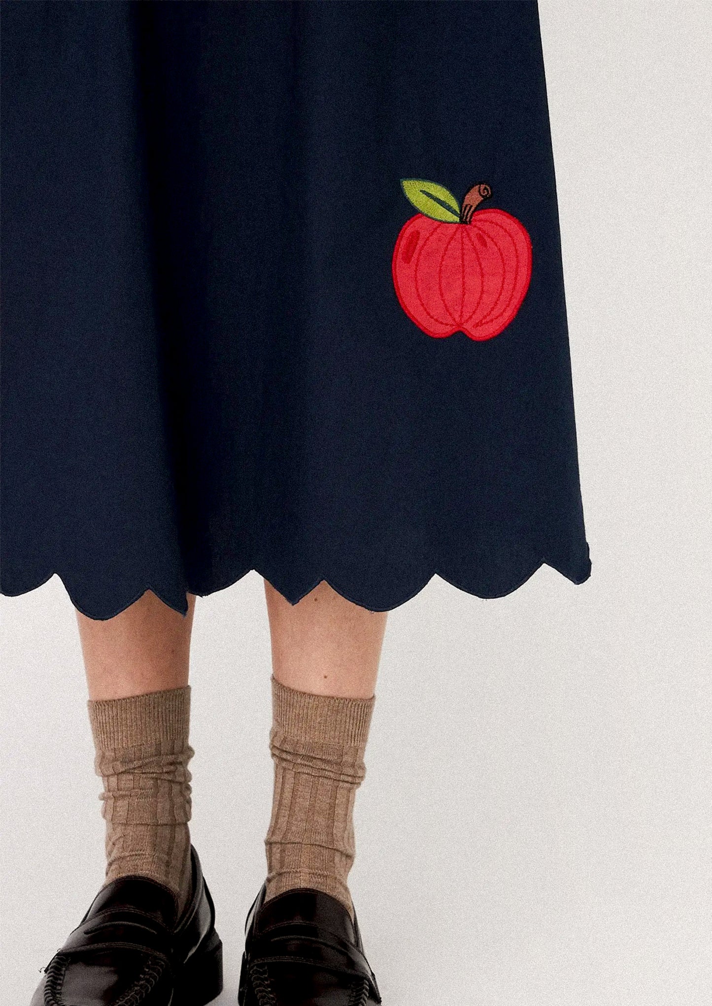 Woman wearing a navy dress with red apple patterns.