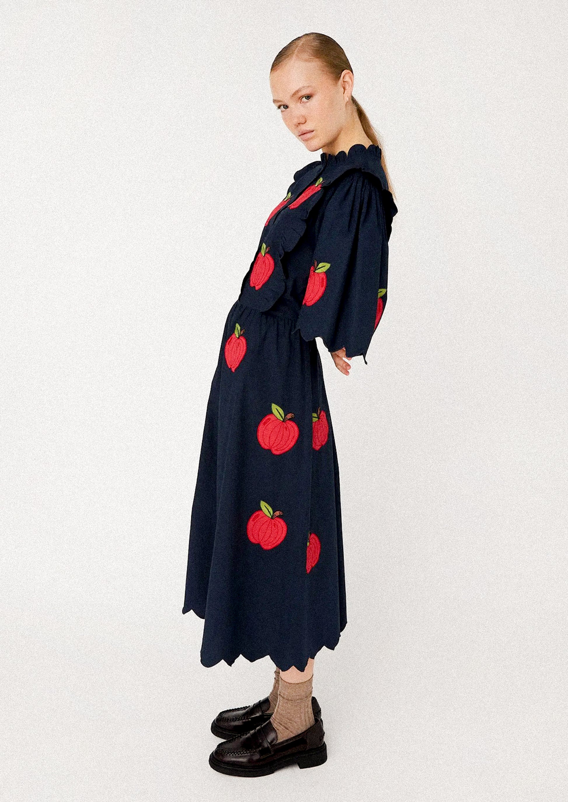 Woman wearing a navy dress with red apple patterns.