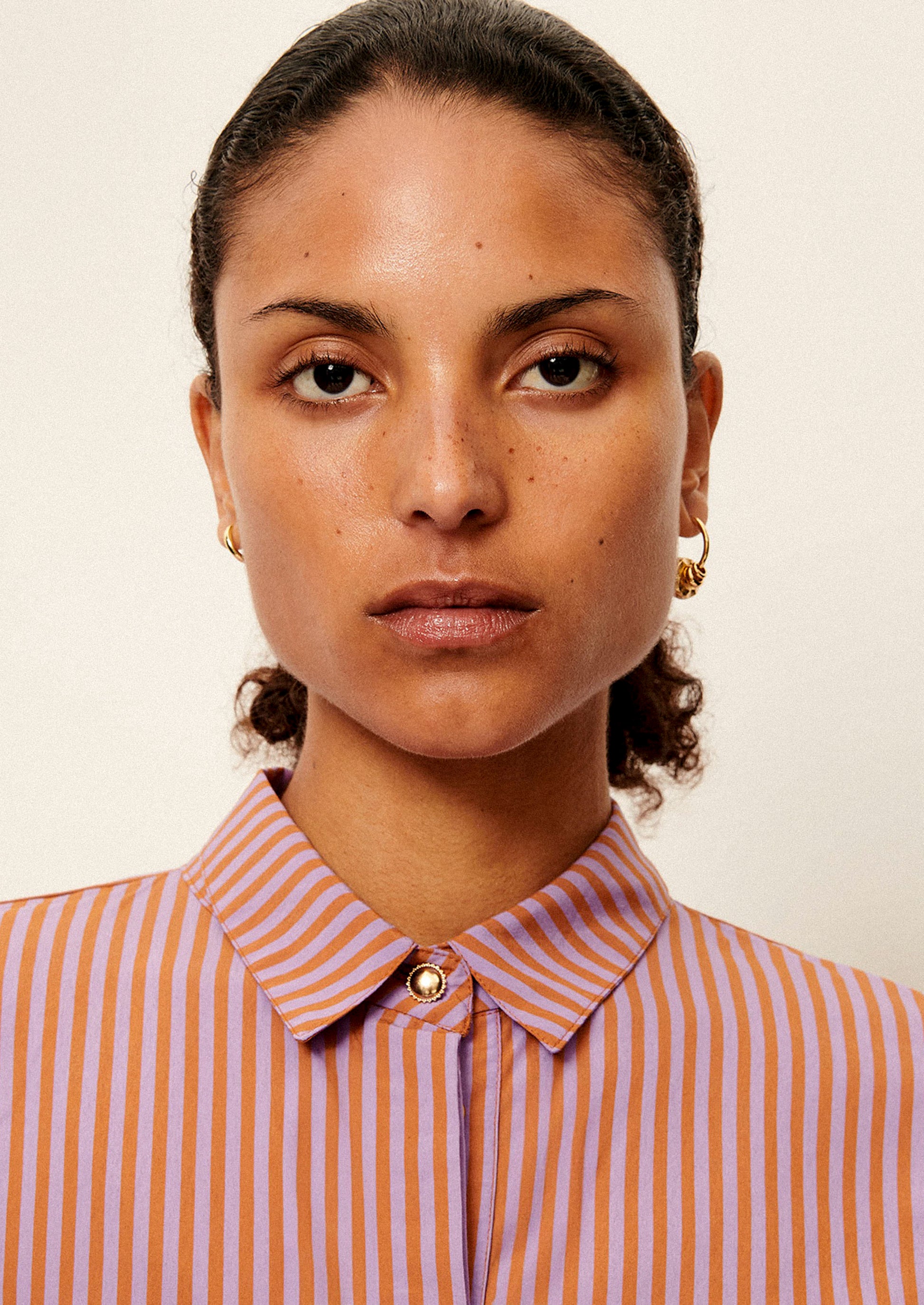 A woman wearing a short collared shirt in orange and purple stripes.