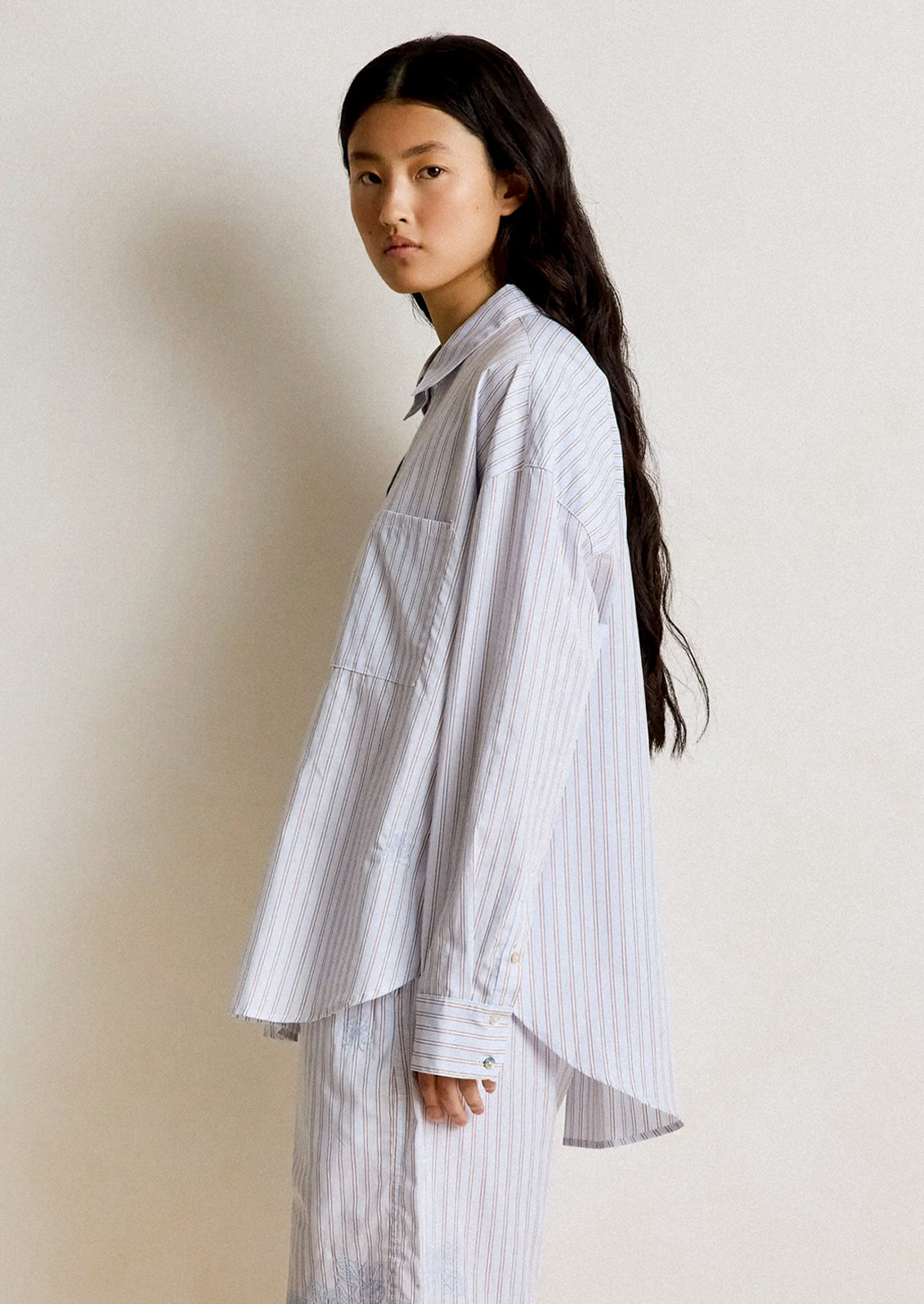 Woman wearing a light-colored striped shirt and pants against a plain background