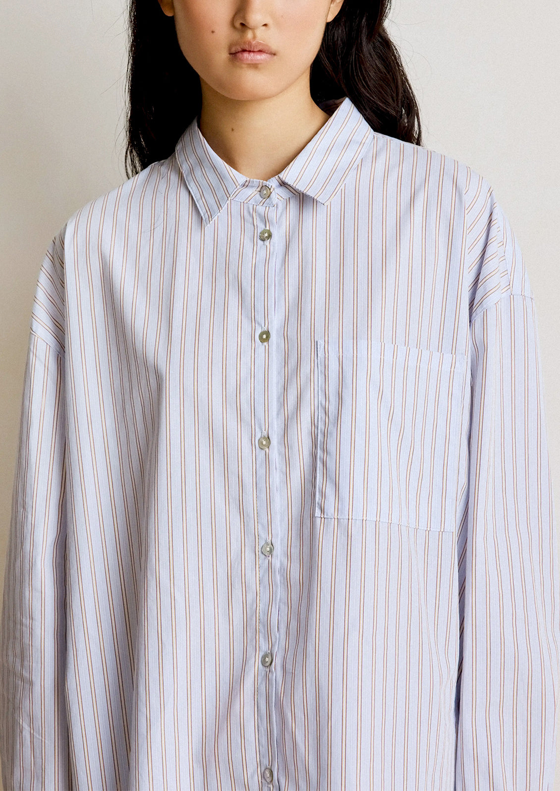 Person wearing a light blue striped shirt against a neutral background