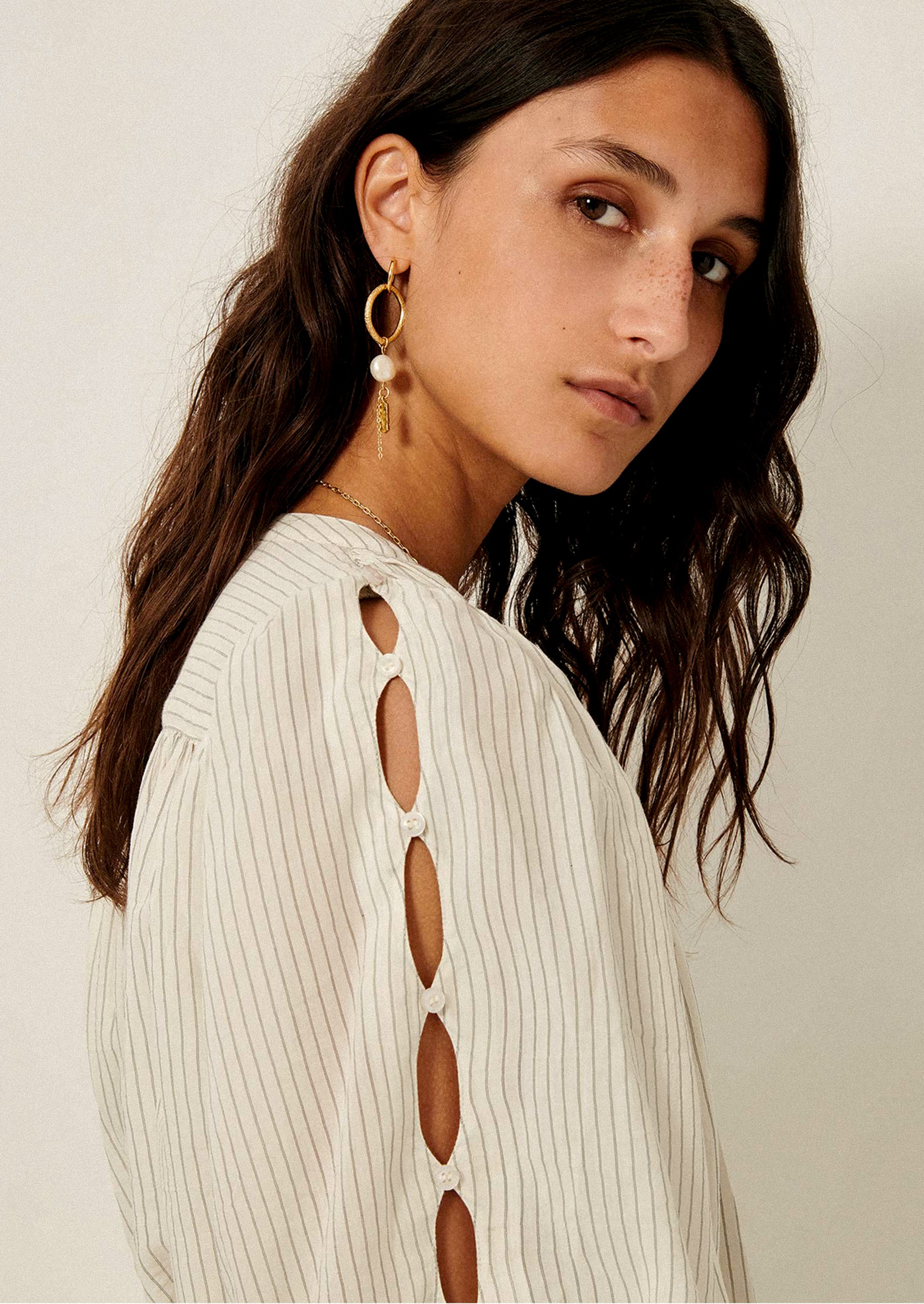 A woman wearing a white blouse with black pinstripe pattern, and cutout detailing on sleeves.