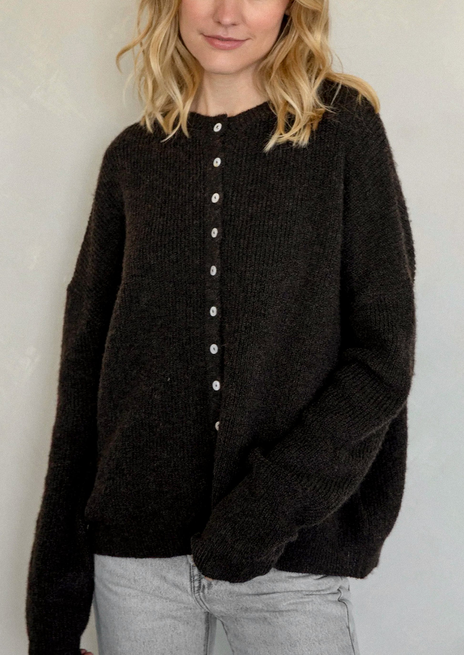 A woman wearing a chocolate brown cardigan with white button front.