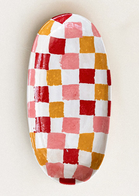 An oval-shaped ceramic platter with sponge painted checker pattern in red, pink and orange.