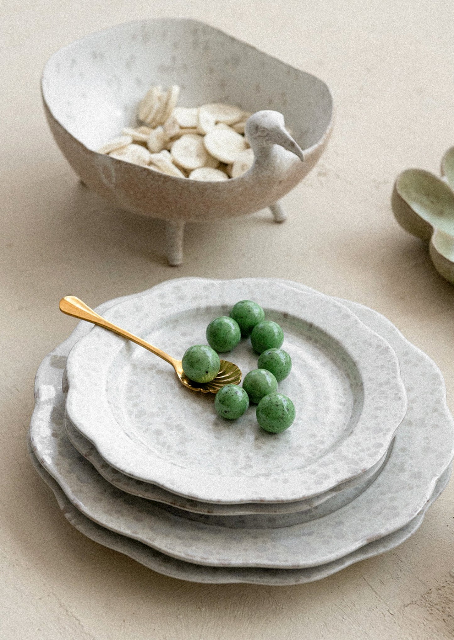 Stack of ceramic plates with green grapes and a gold spoon on a light surface.