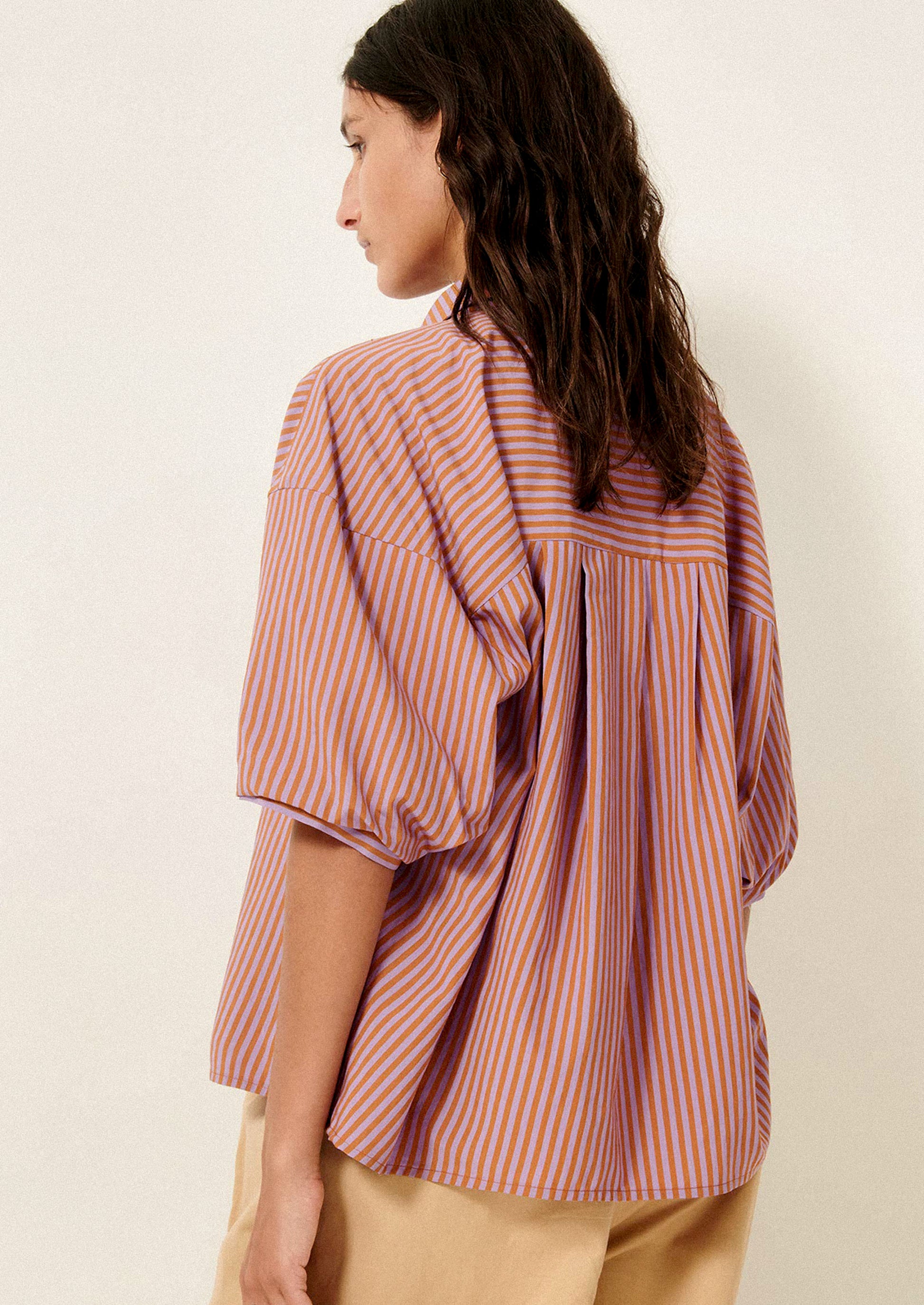 A woman wearing a short collared shirt in orange and purple stripes.