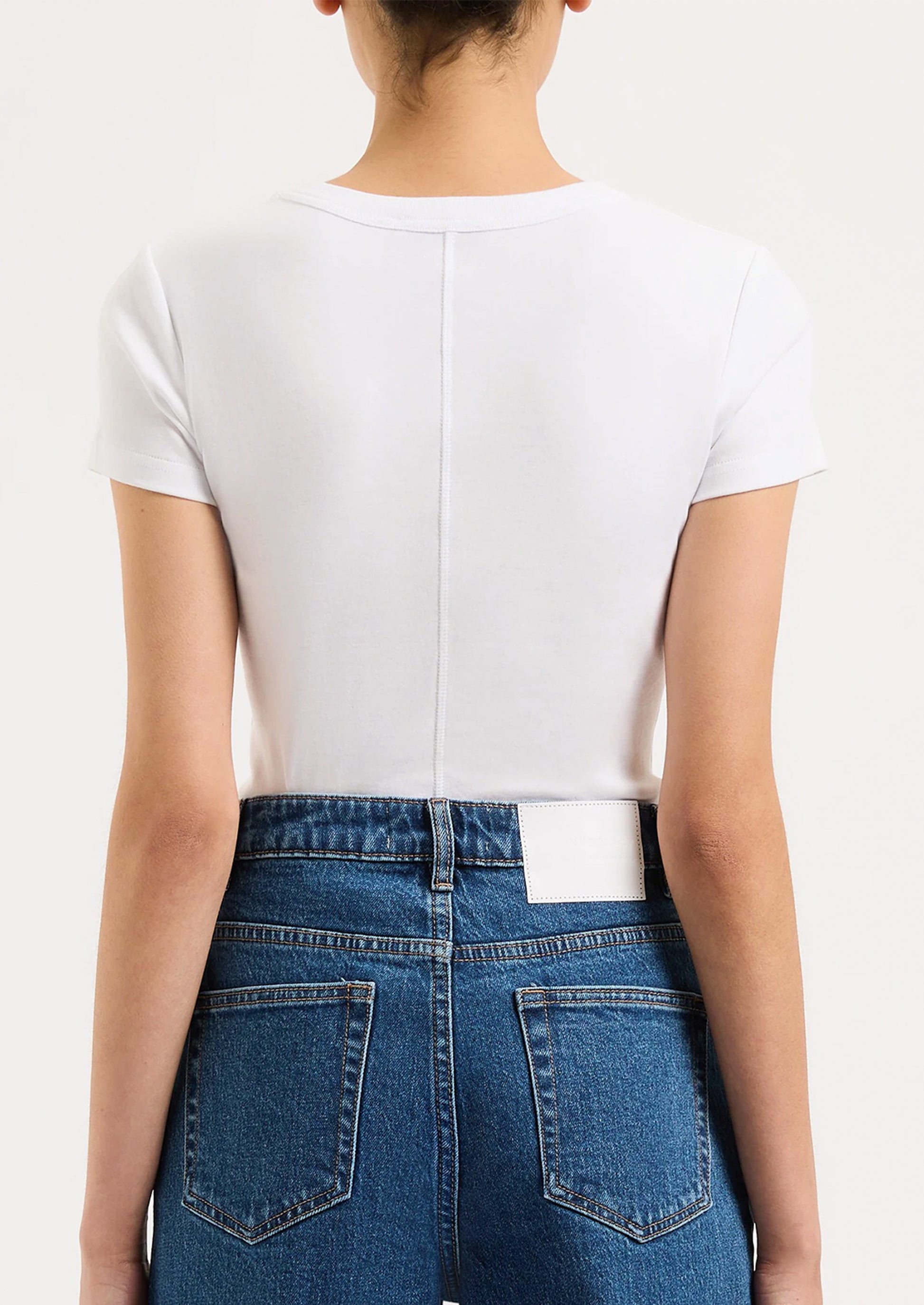 A person wearing a solid white fitted baby tee with tonal seam down back.