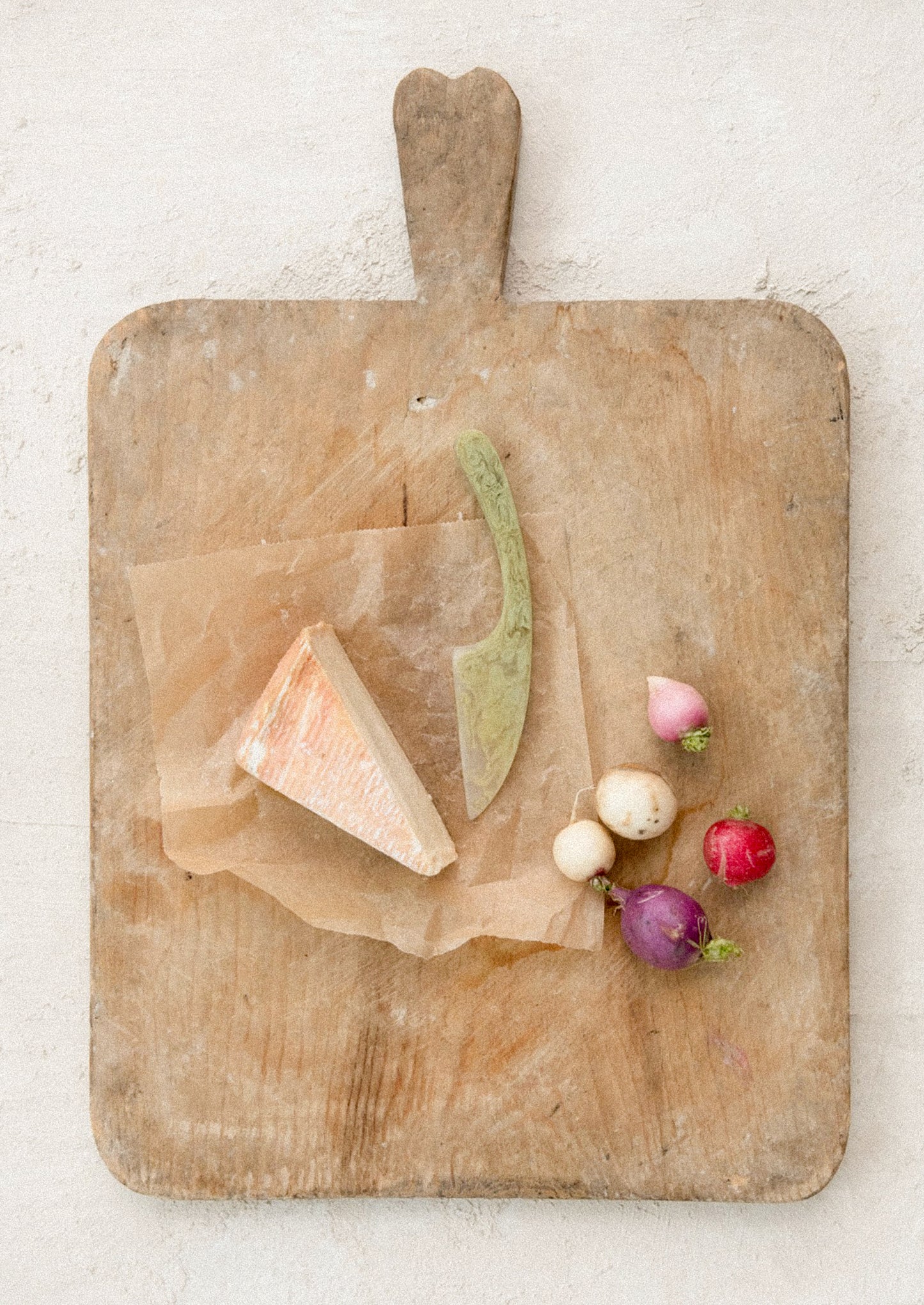 Wooden cutting board with cheese, a knife, and radishes on a light background