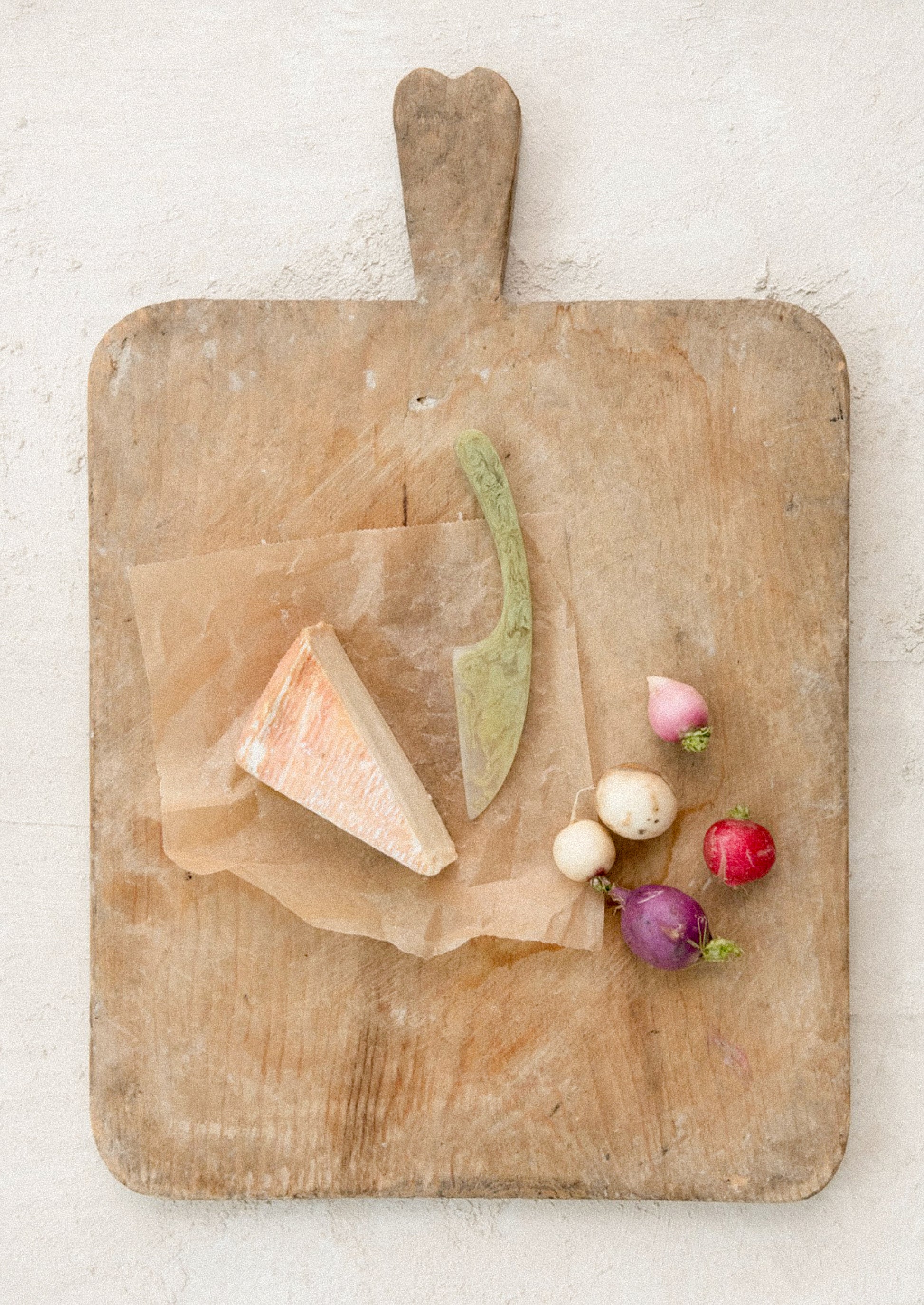 Wooden cutting board with cheese, a knife, and radishes on a light background