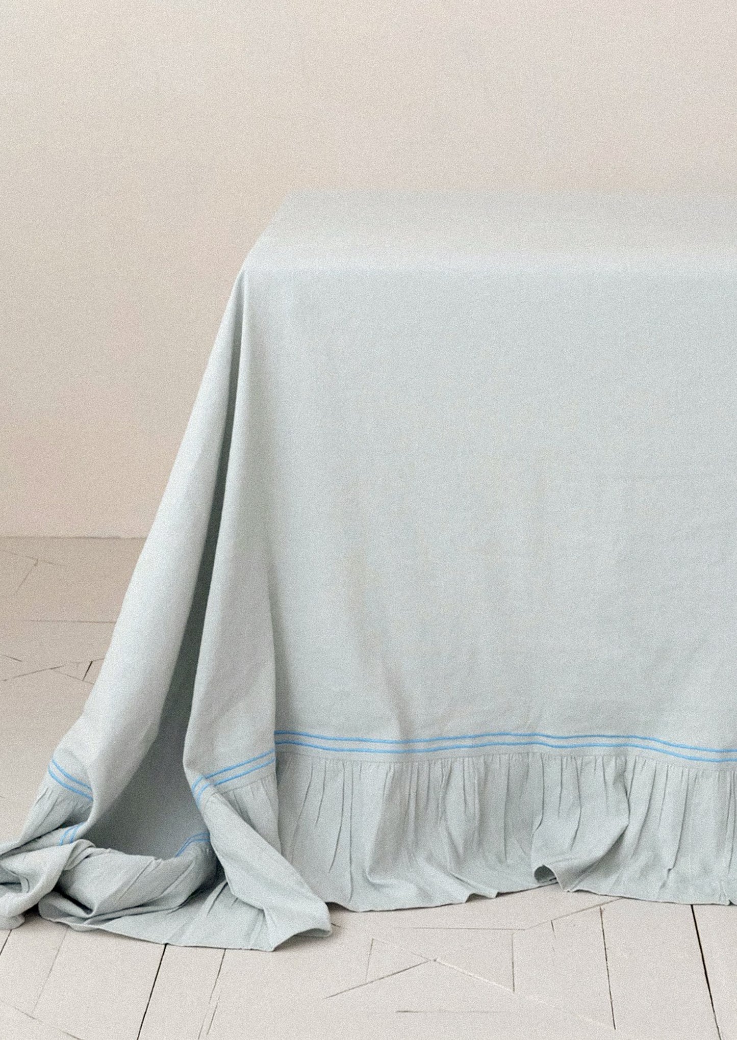 Light blue tablecloth draped over a table on a wooden floor with a neutral wall background