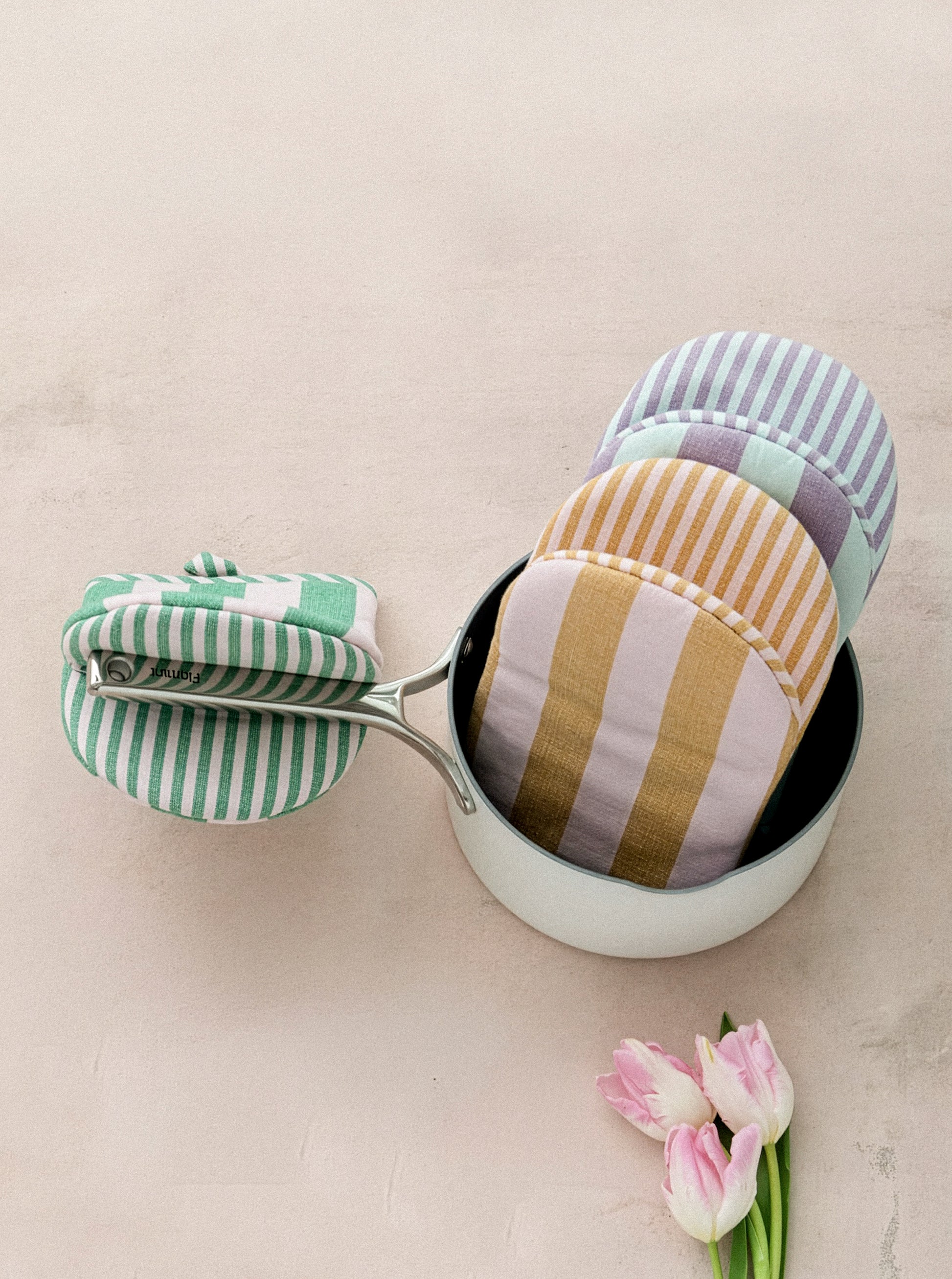 Striped fabric items in a white container on a beige surface with pink tulips.