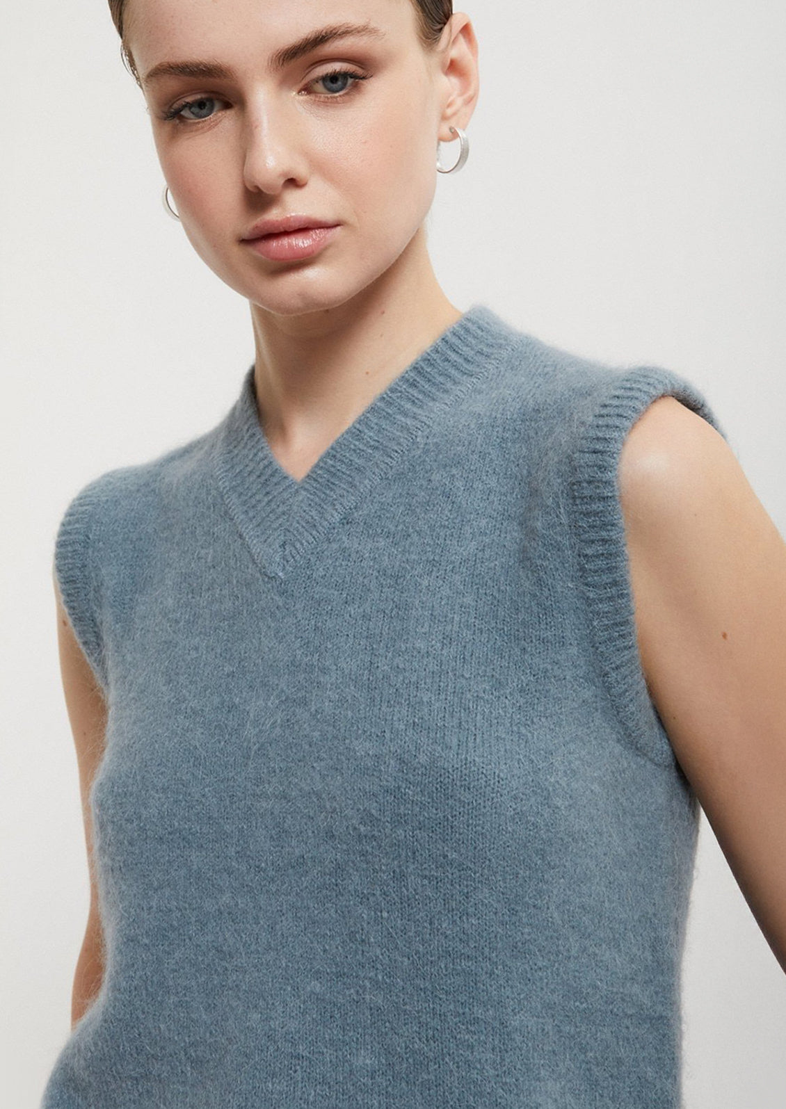 Woman wearing a light blue sleeveless sweater against a plain background