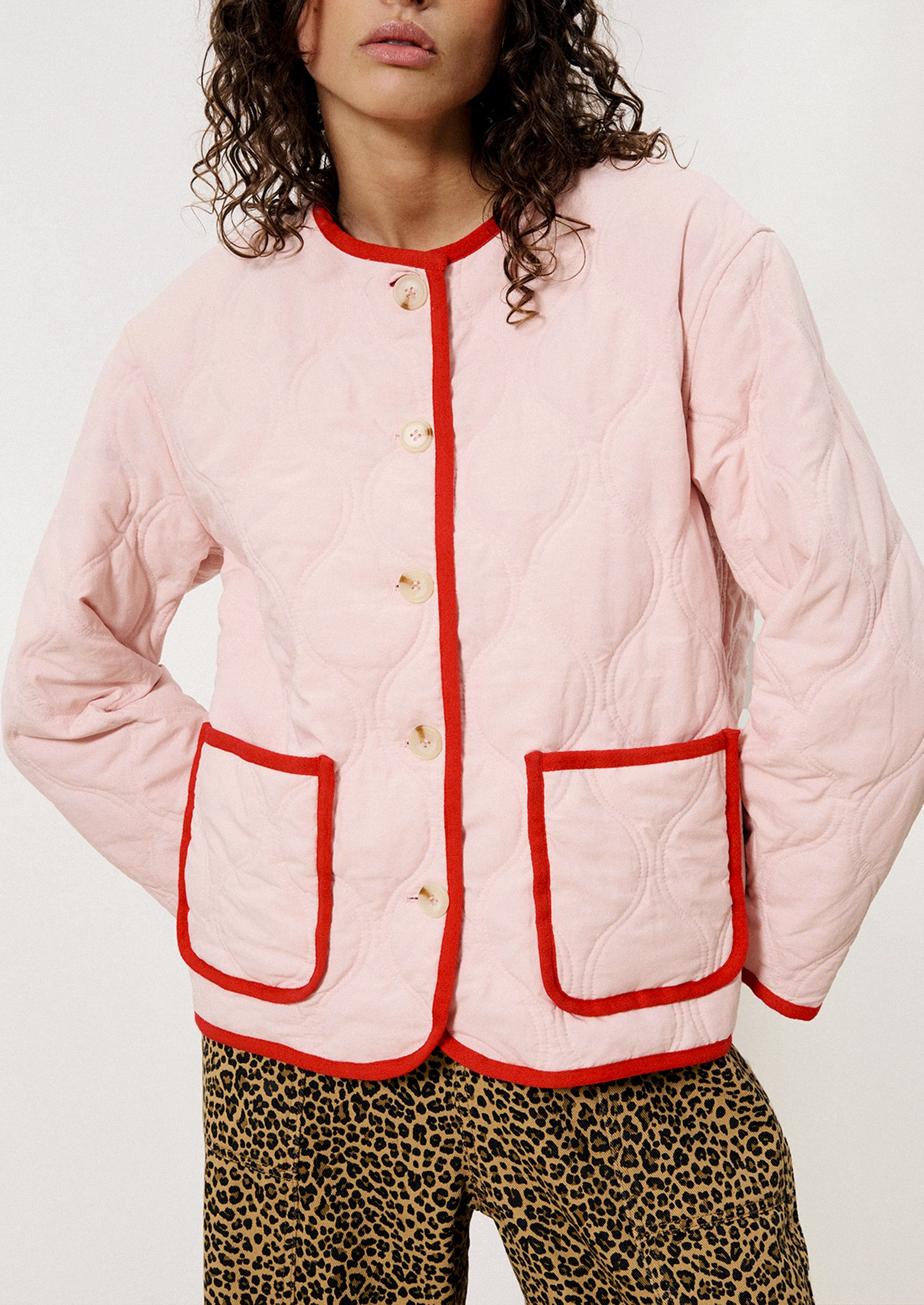 A person wearing a pink quilted jacket with red trim.
