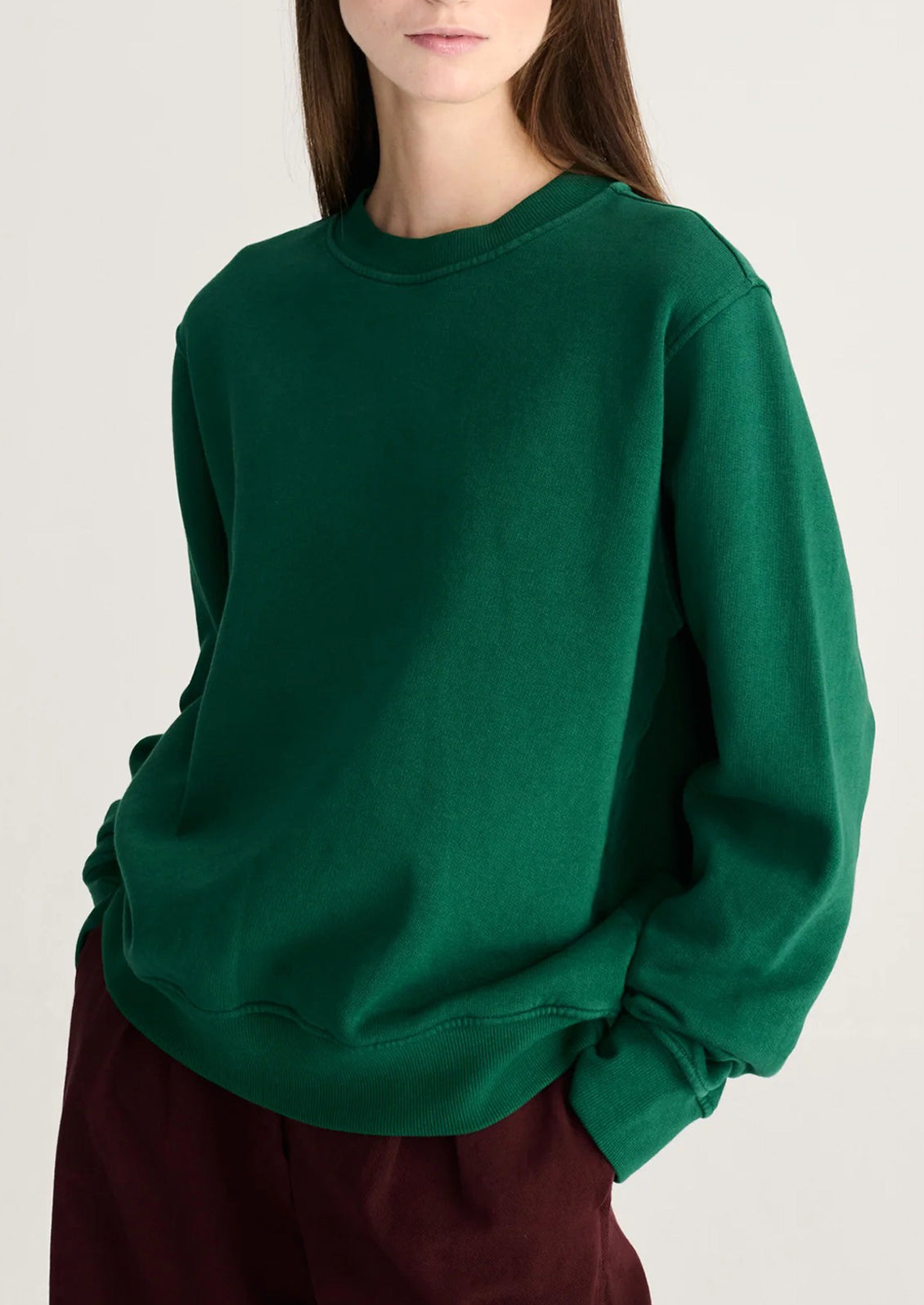 A woman wearing a dark green crewneck sweatshirt and burgundy pants, cropped from the mouth down against a plain light background.