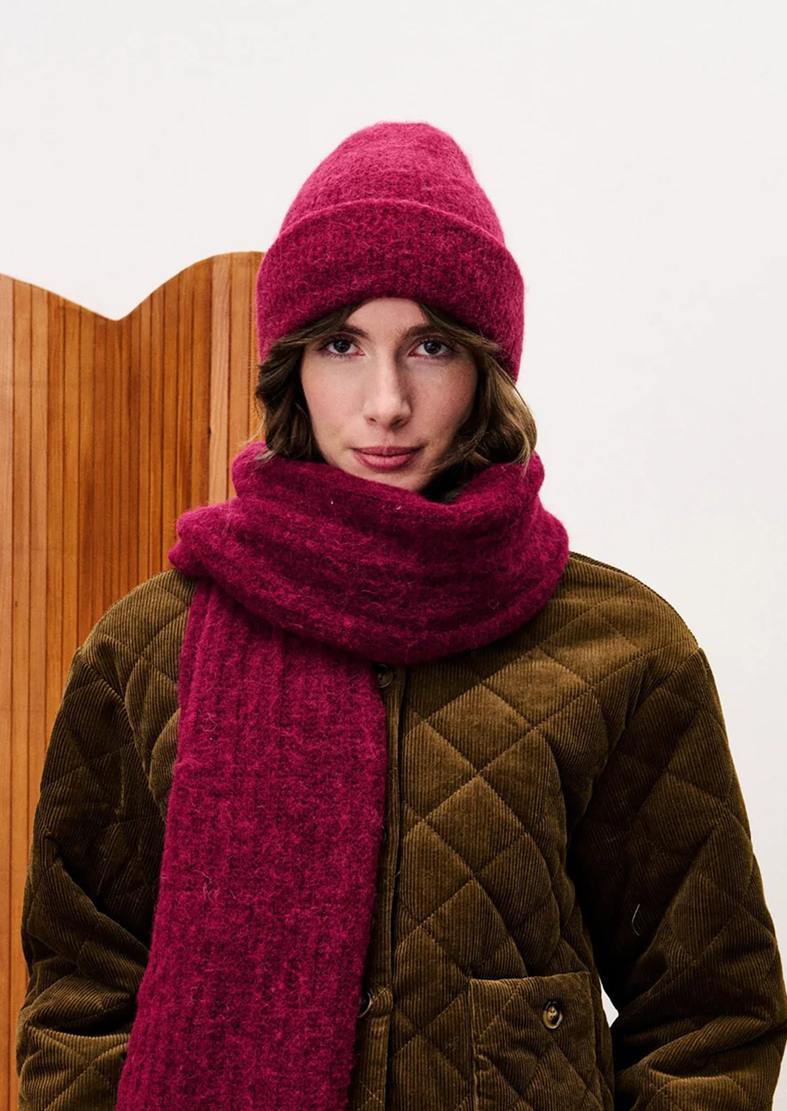 Person wearing a burgundy knitted hat and scarf against a white background