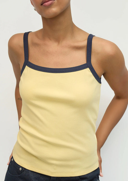 Woman wearing a yellow tank top with navy straps on a plain background
