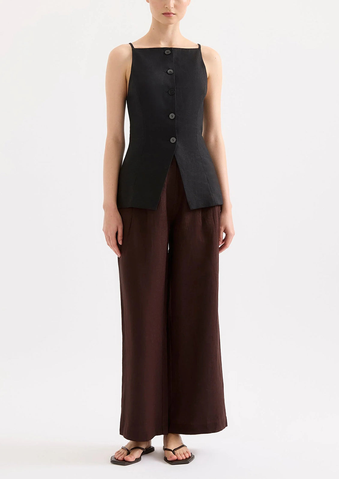 Person wearing a black sleeveless top and brown wide-leg pants on a white background