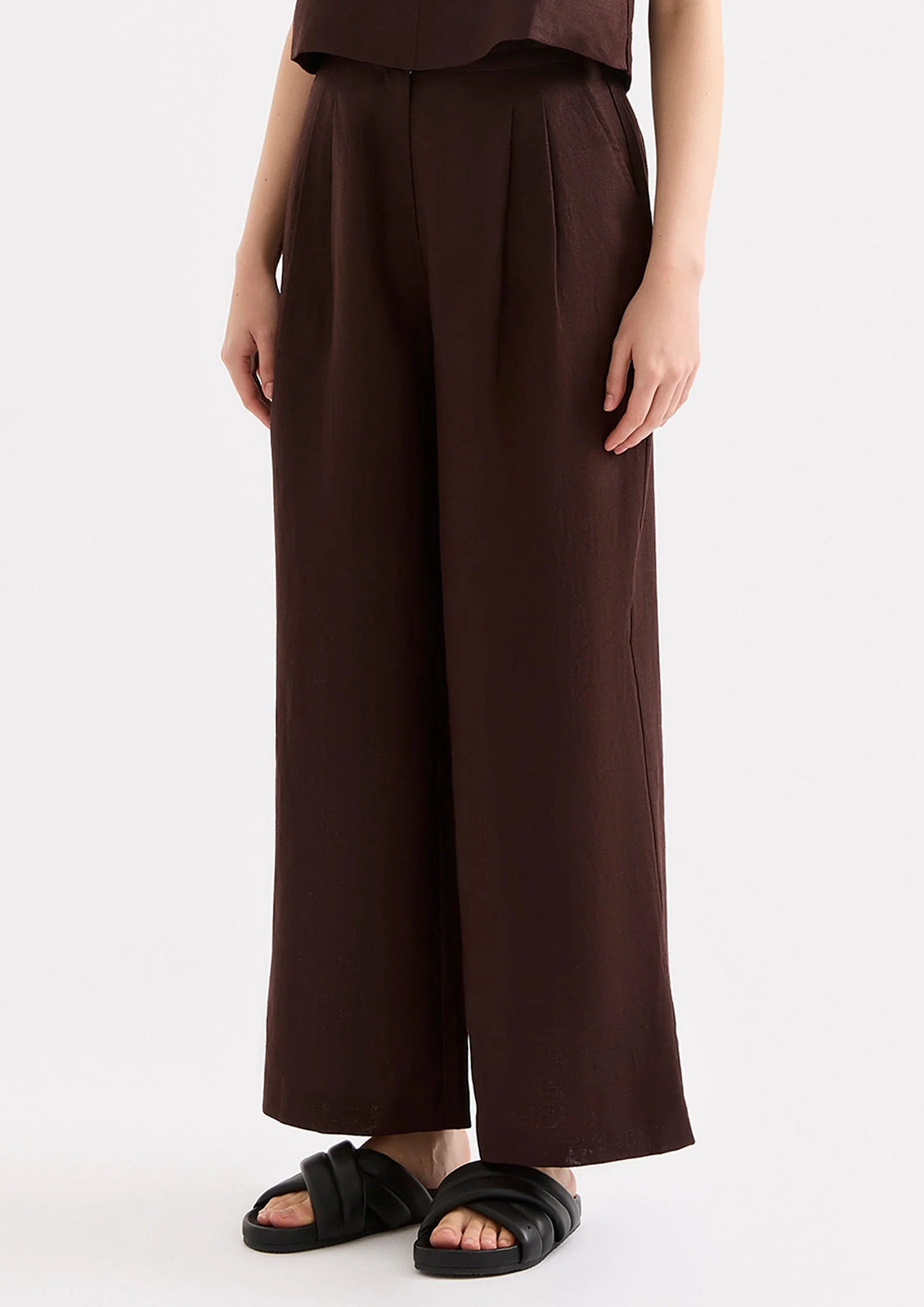 Person wearing brown wide-leg pants and black sandals on a white background