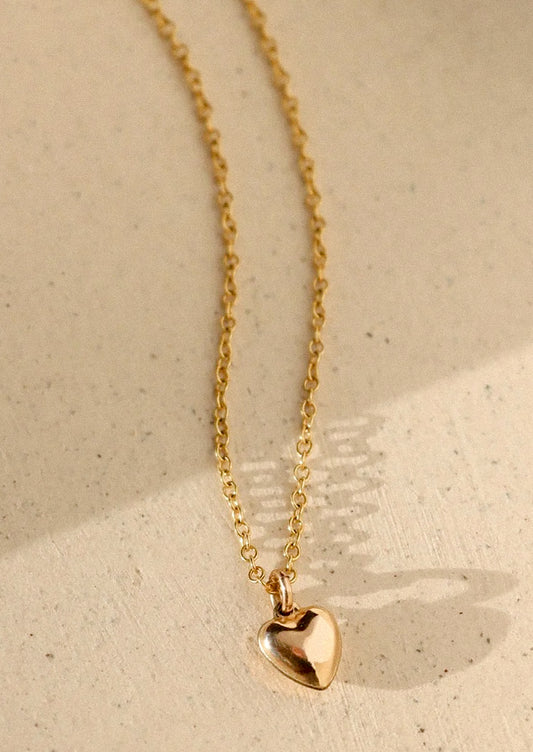 Gold heart-shaped pendant necklace on a beige background